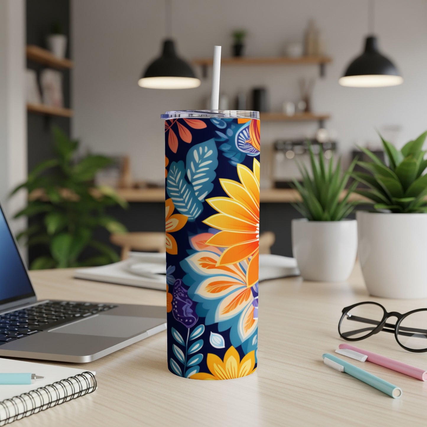 Tall tumbler with colorful floral design on a desk with laptop and pens.