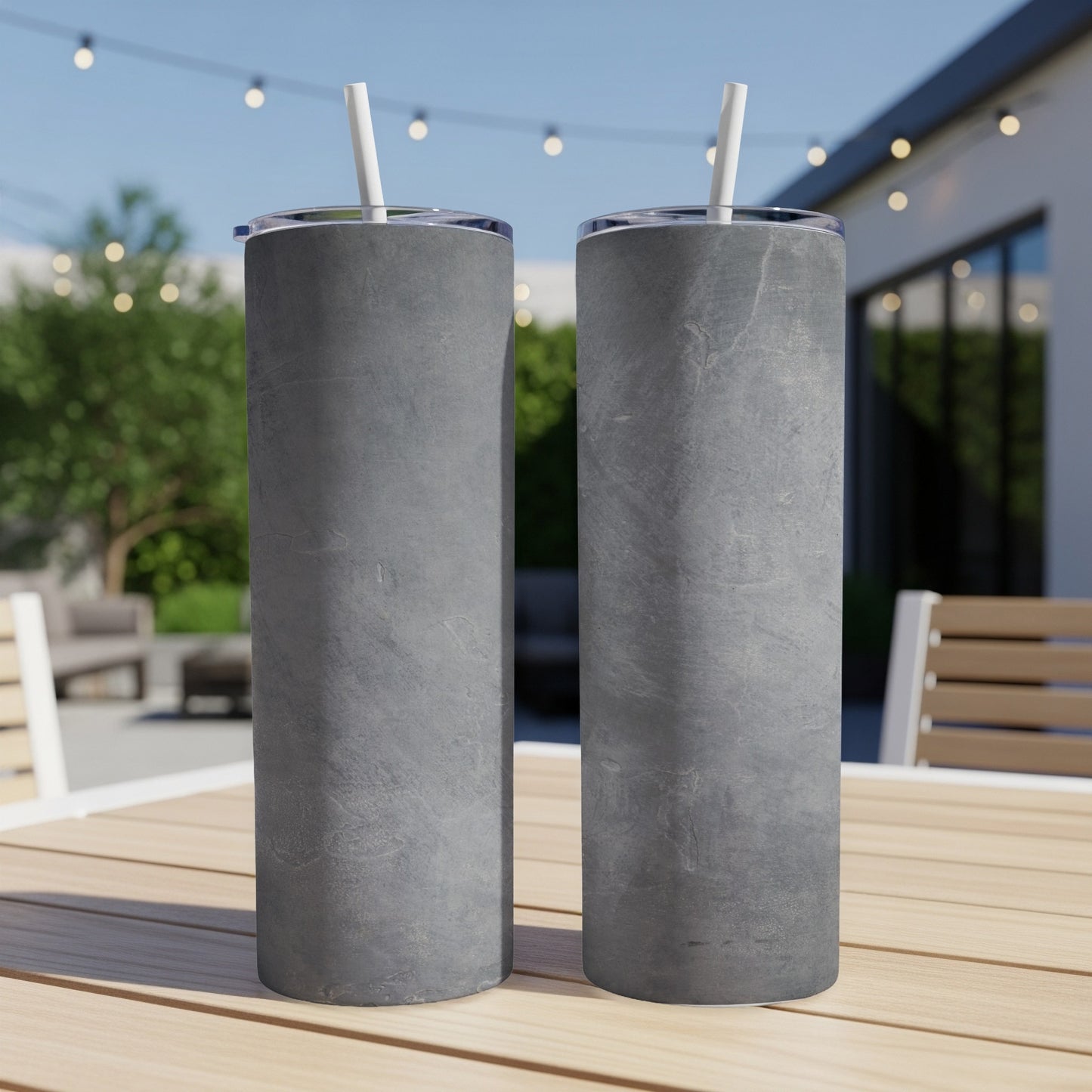 Two gray textured tumblers with straws sit on a wooden table outdoors.
