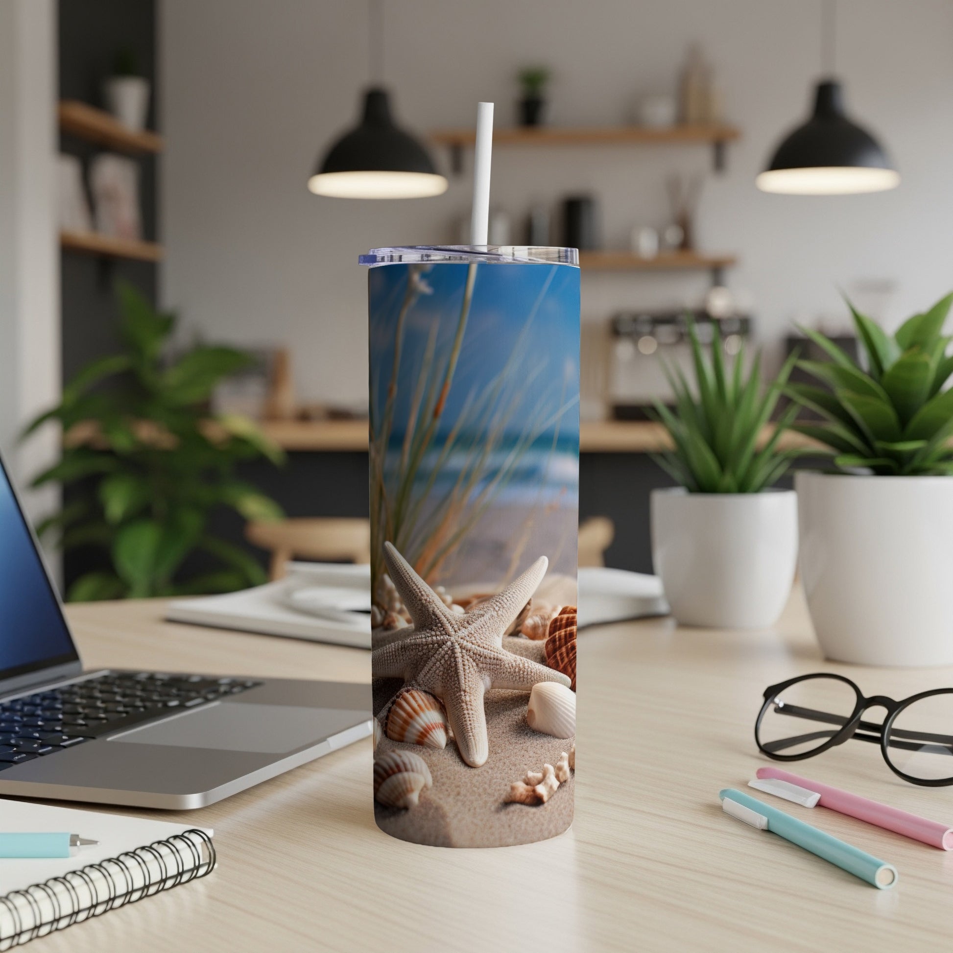 Beach-themed tumbler with seashells and seagrass on sand, on a desk.