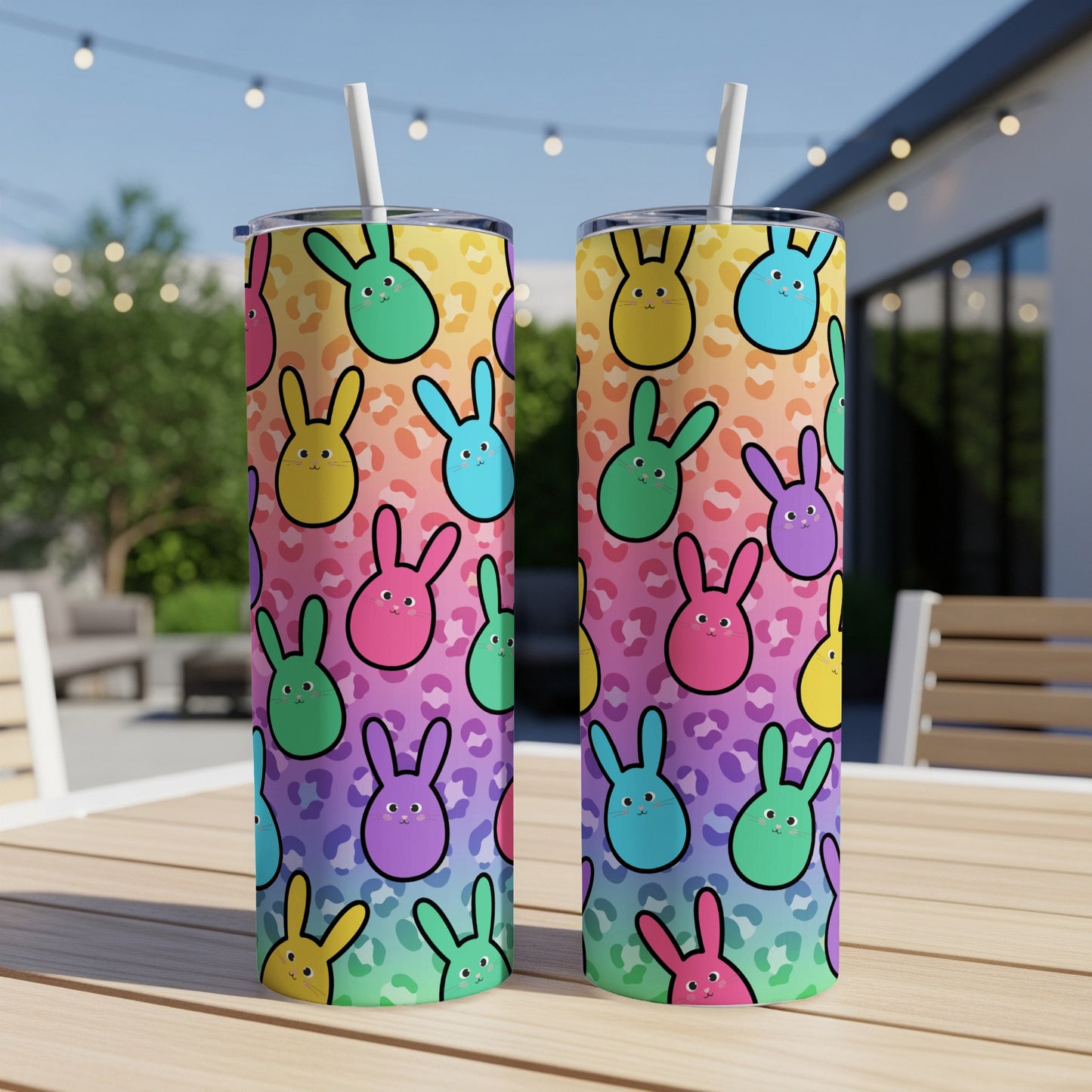 Two colorful bunny-patterned tumblers with straws on an outdoor table.