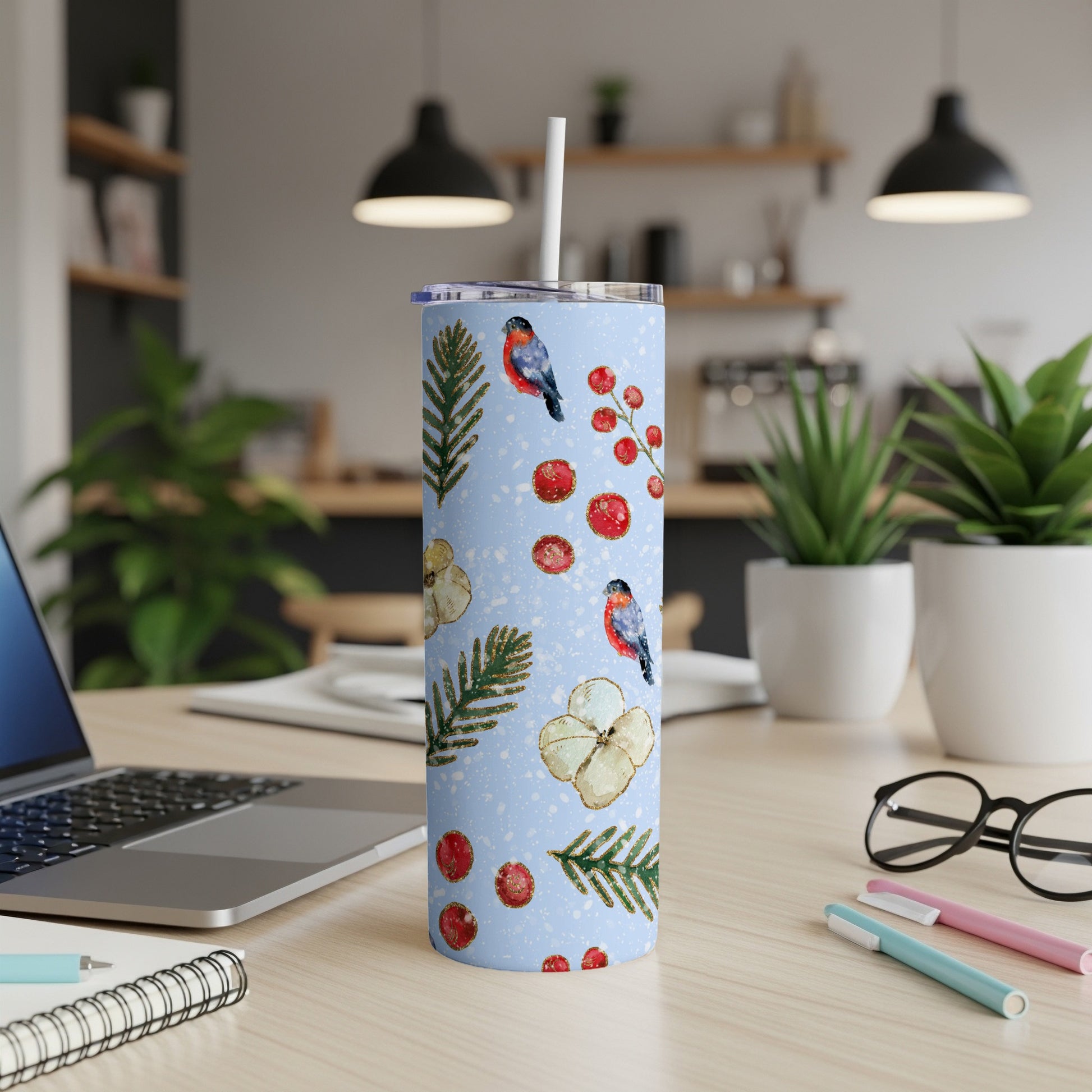 Blue tumbler with pine branches, berries, and birds, set on a desk.