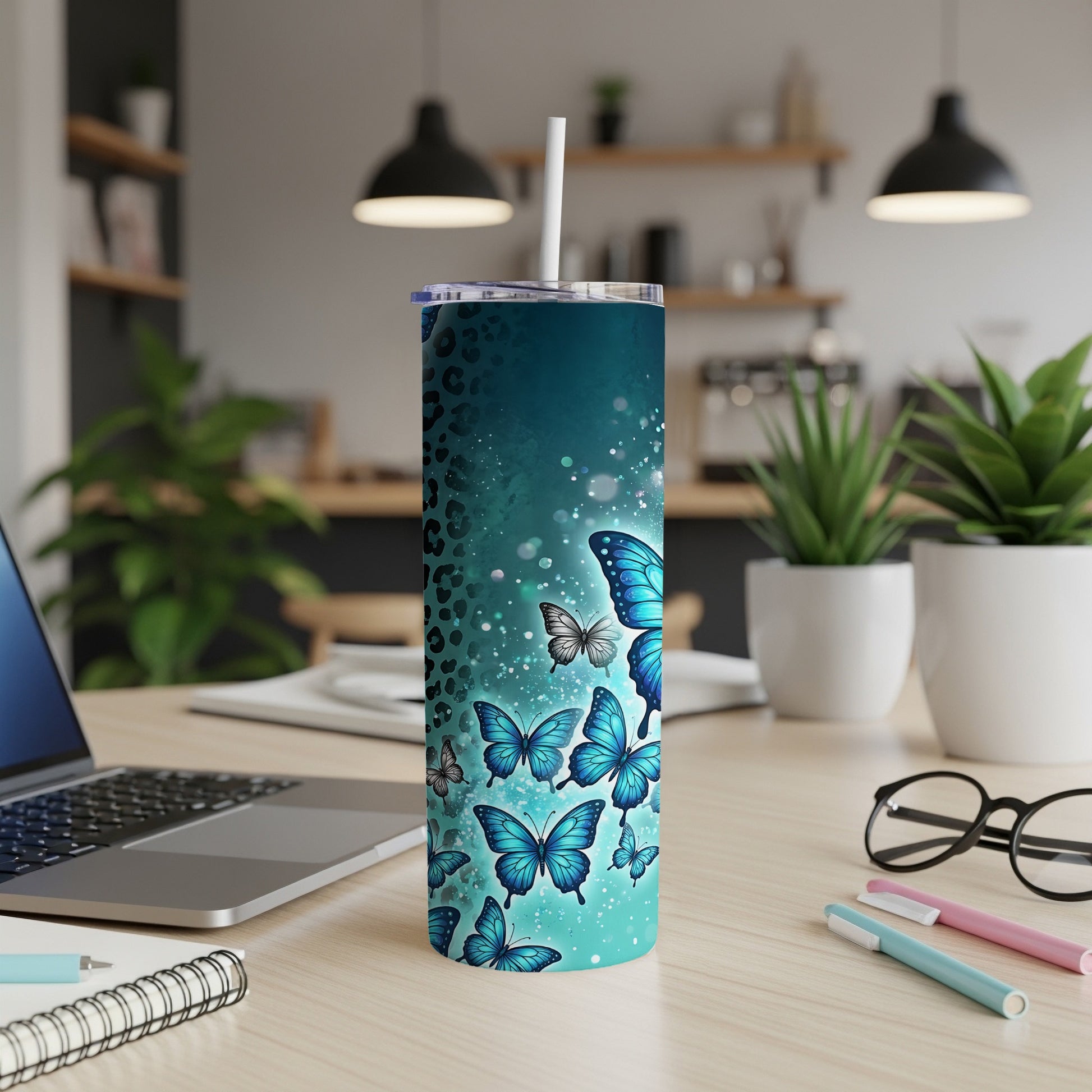 Blue butterfly tumbler with straw on a desk with laptop and pens.