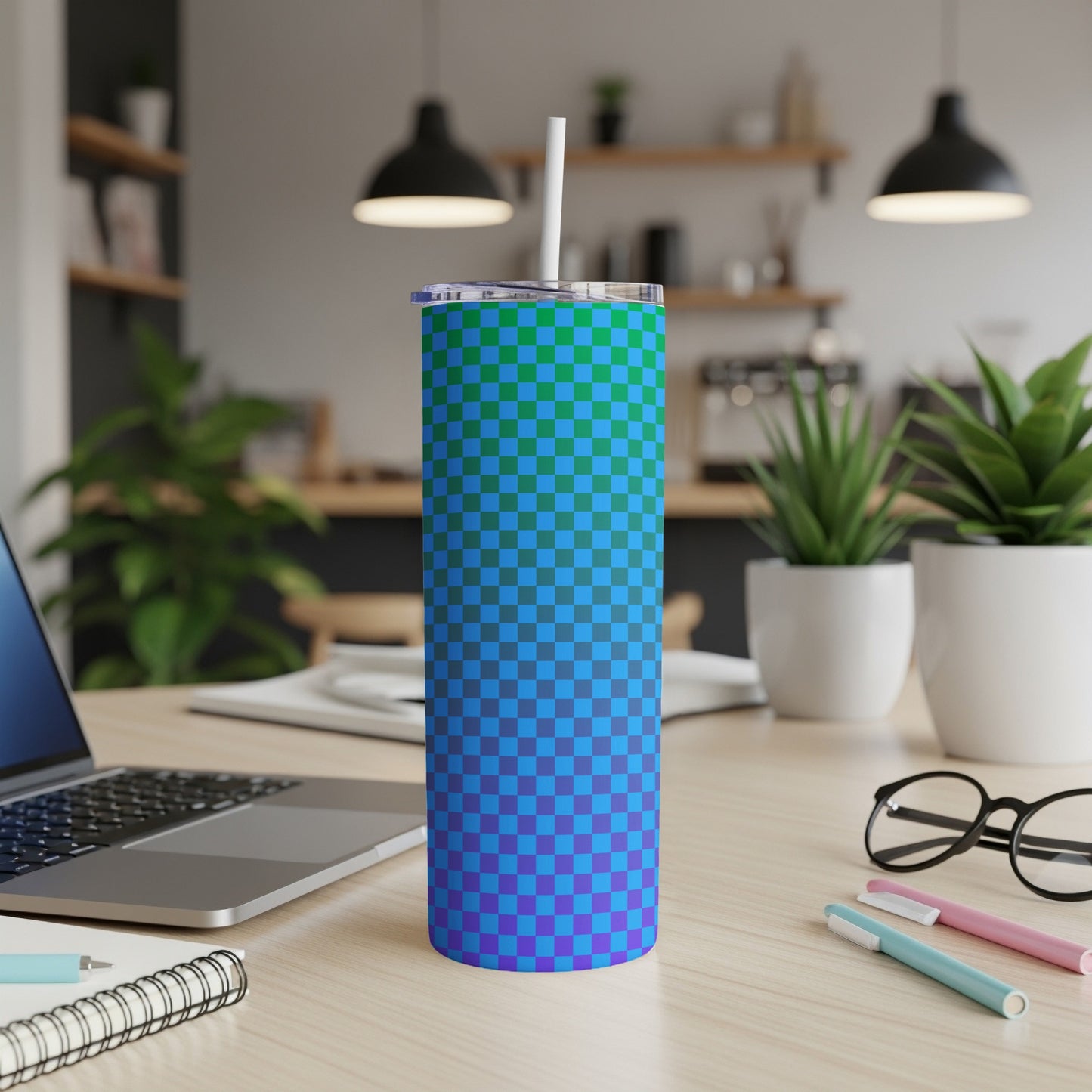 Blue and green checkered tumbler with straw on a desk.
