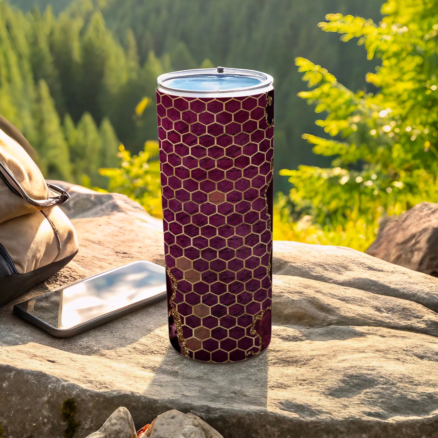 Maroon honeycomb tumbler with gold accents on rocky outdoor surface.