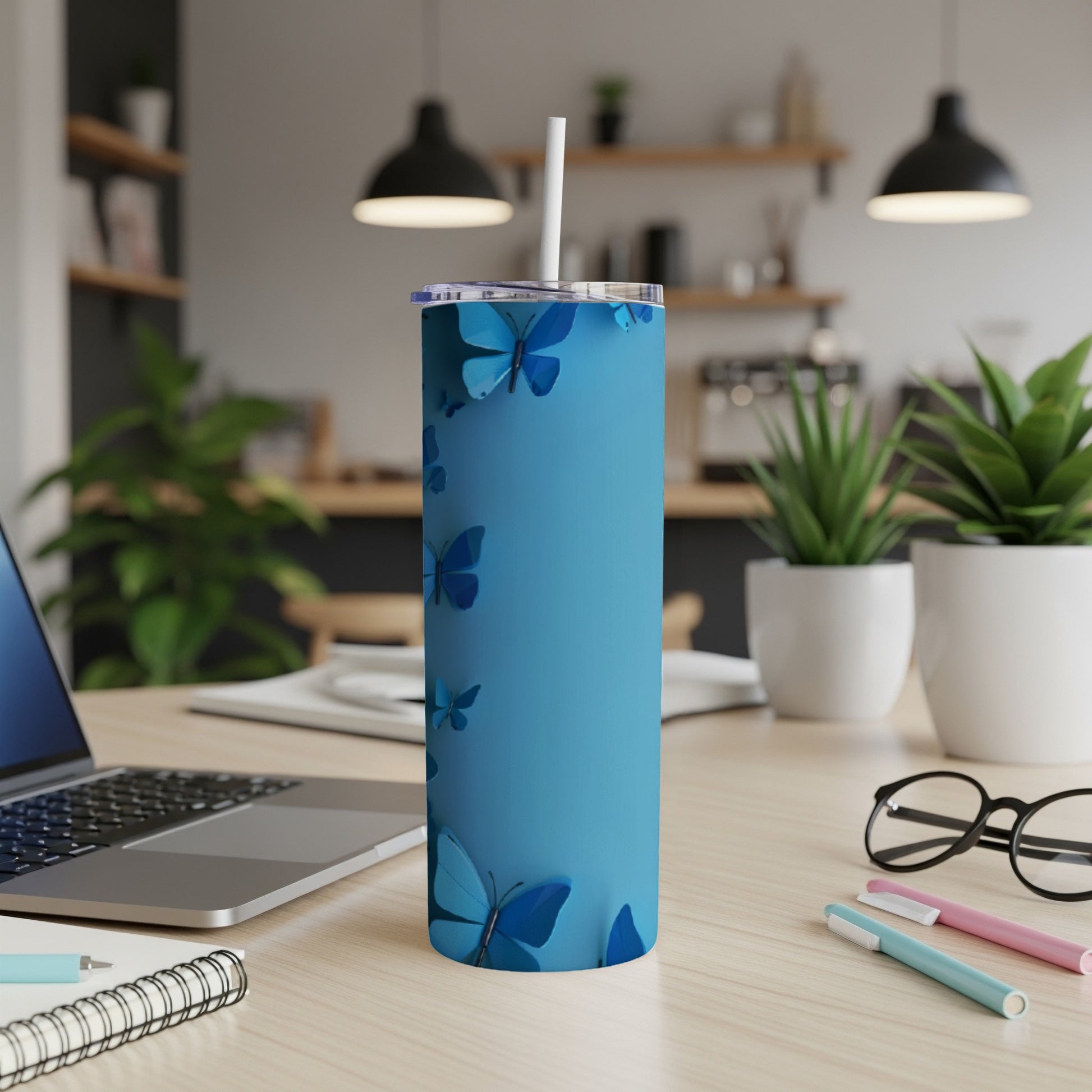 Blue tumbler with scattered butterfly designs, on a desk with laptop and pens.