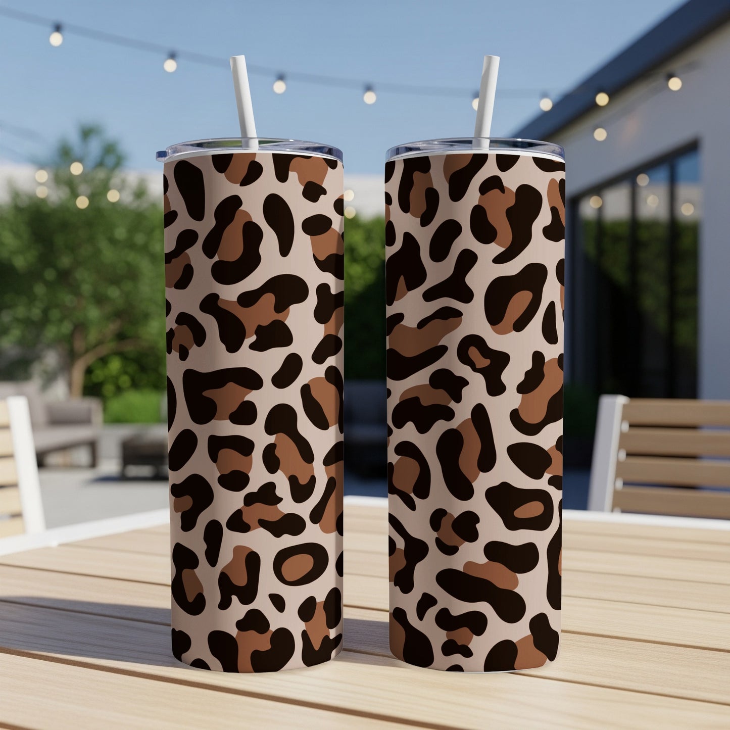 Two leopard print tumblers with white straws standing on a wooden table.