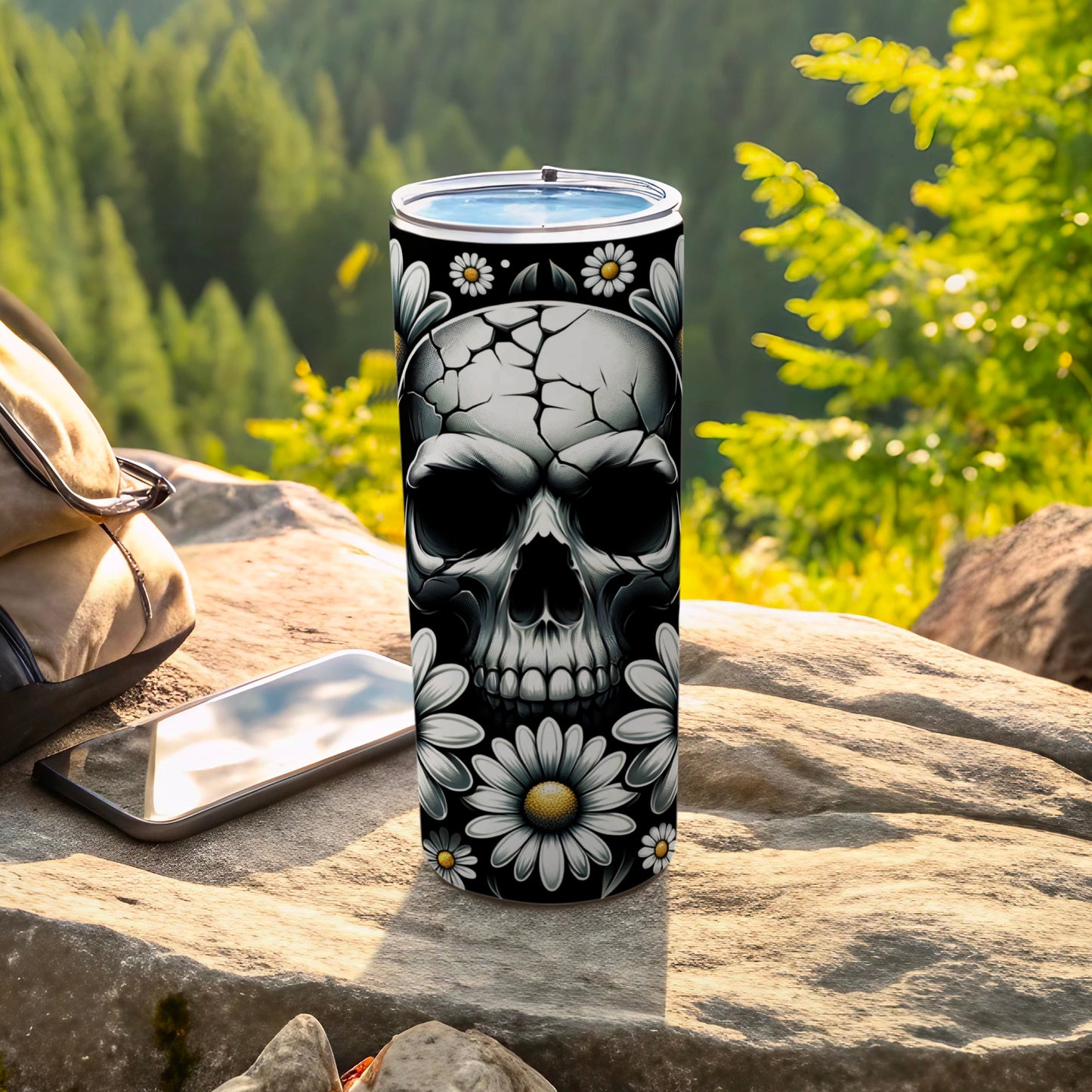 Black tumbler with skull and daisy pattern on rocks with phone.
