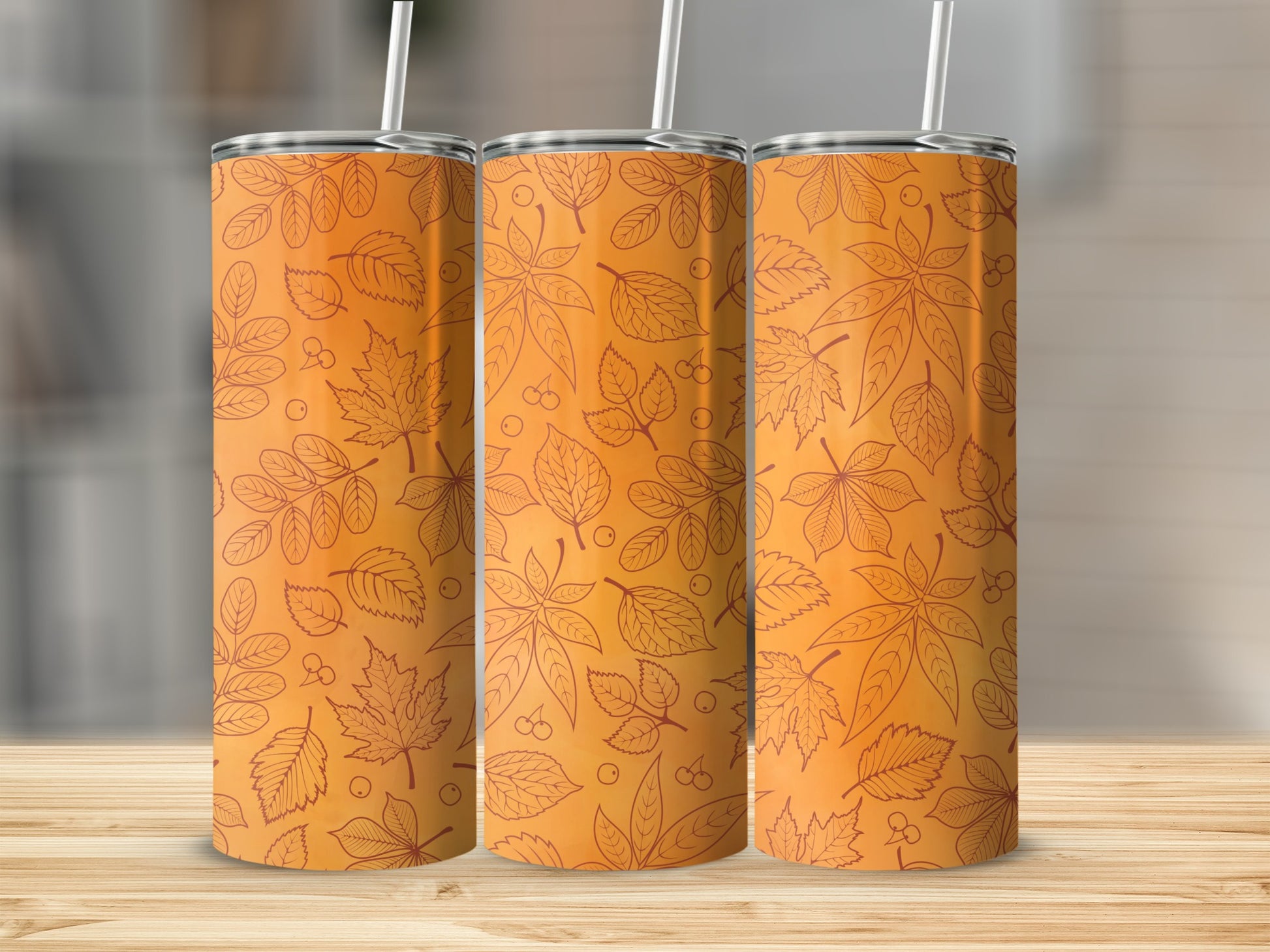 Three orange tumblers with a fall leaf pattern on a wooden surface.