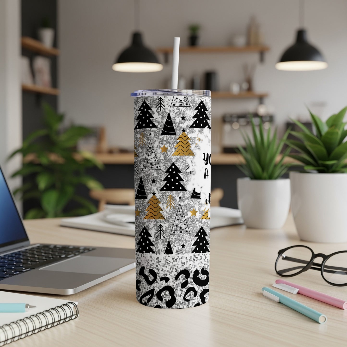 White tumbler with Christmas trees and glitter patterns, straw, on a desk.
