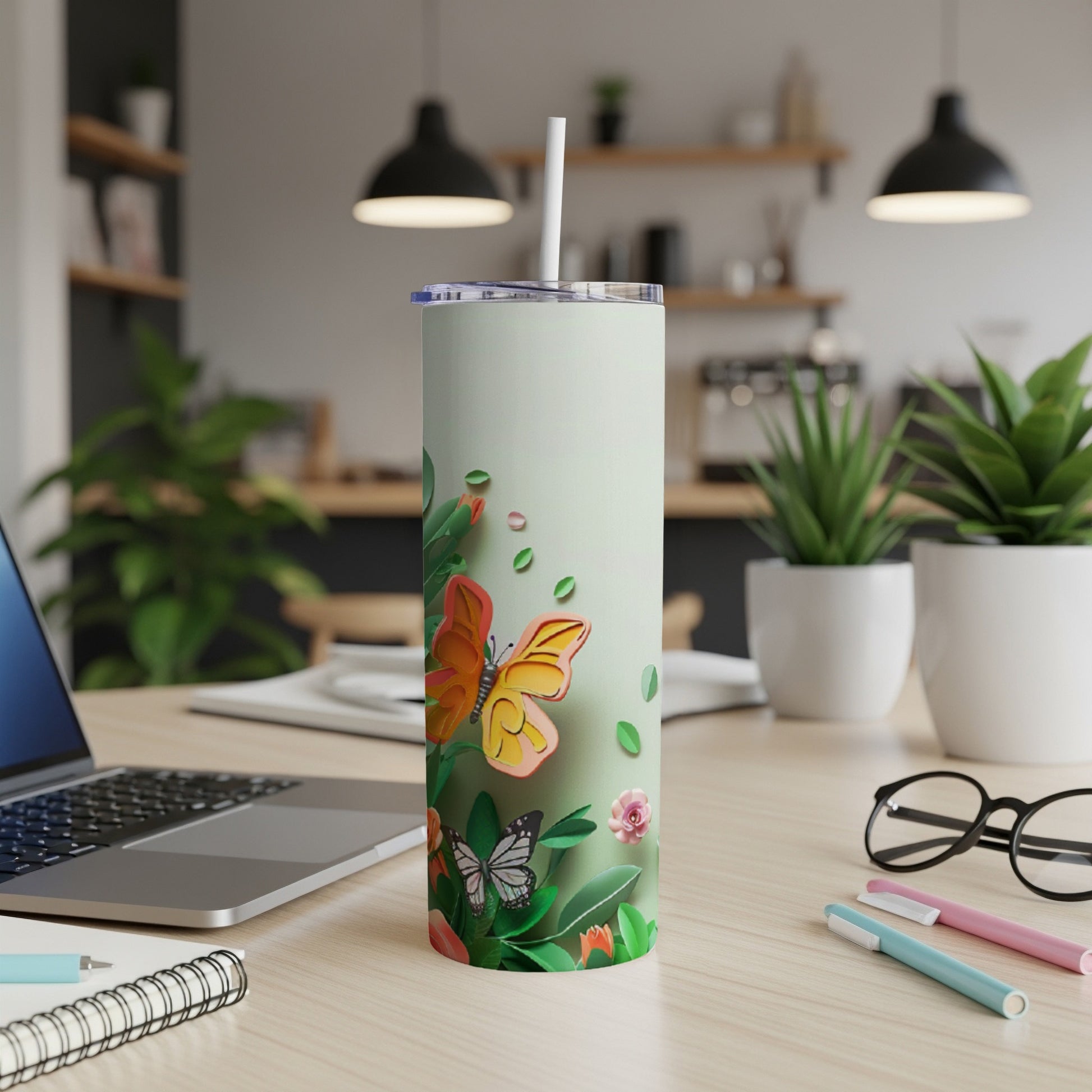 Tall tumbler with butterfly and floral design on a desk.