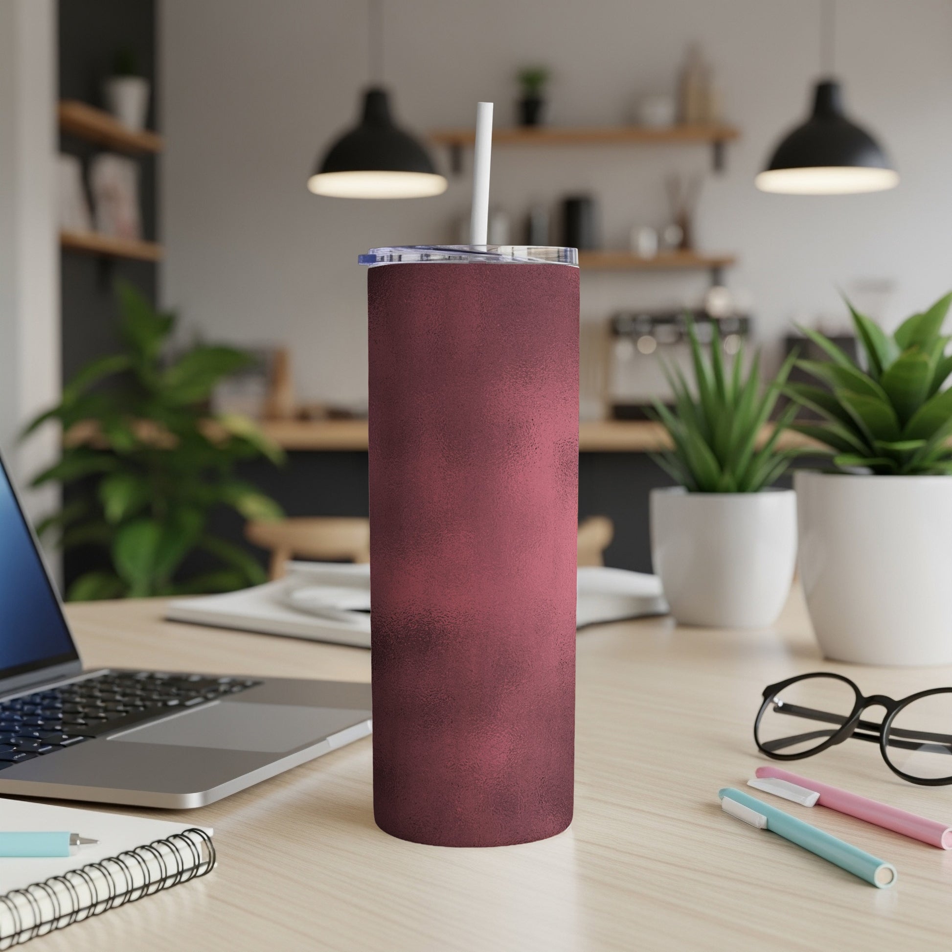 Maroon textured tumbler with white straw on a desk with laptop and plants.