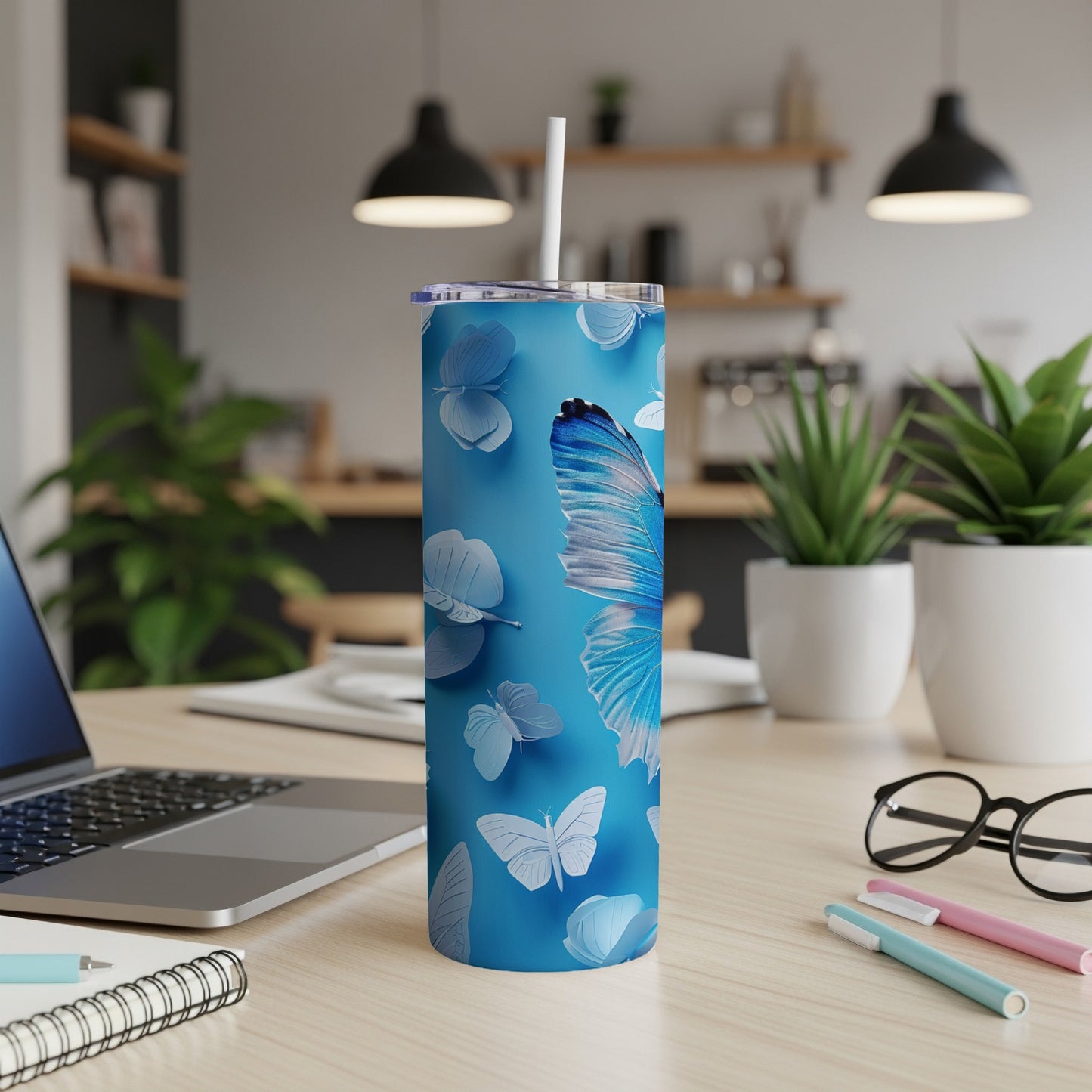Blue tumbler with white butterflies and a straw on a desk.