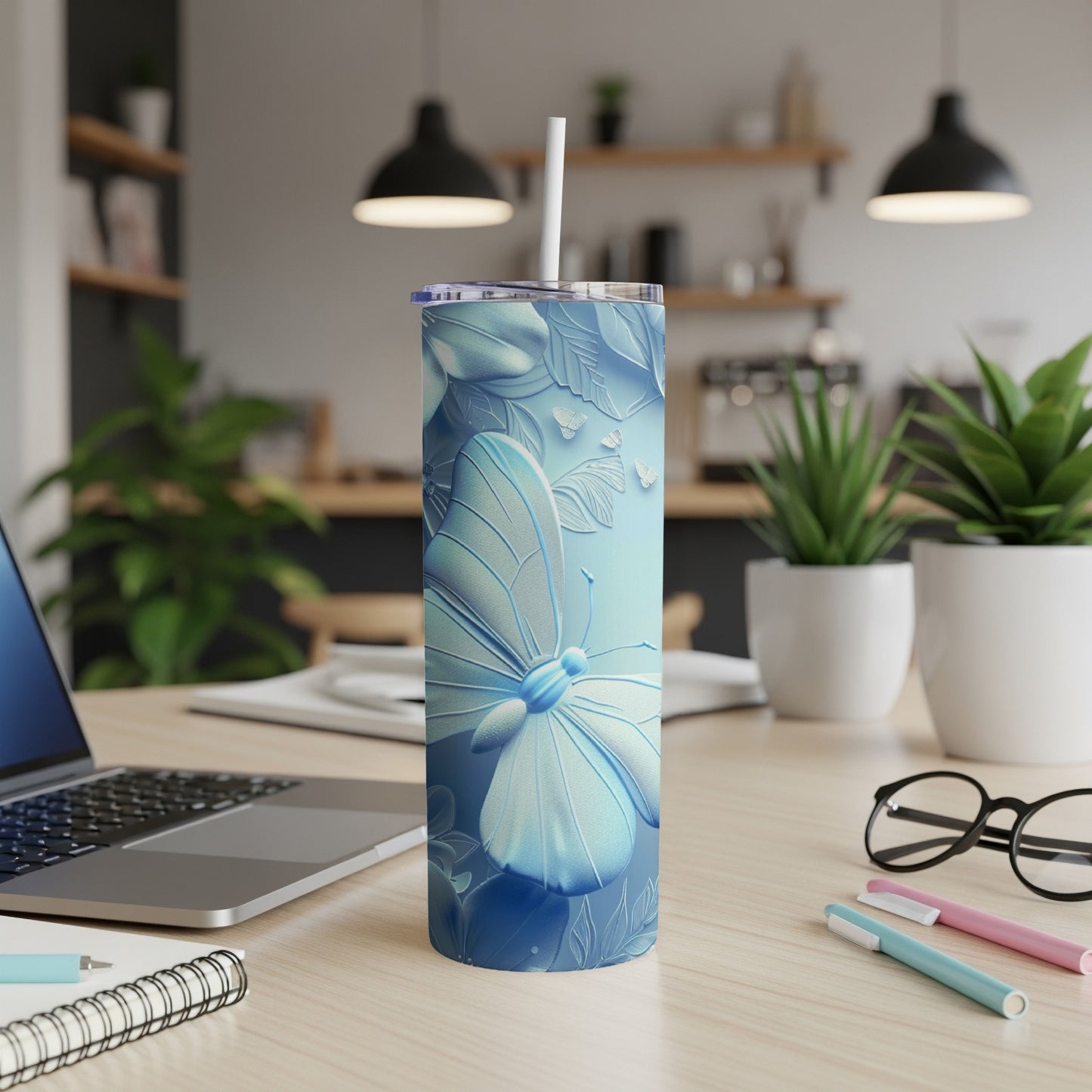 Blue butterfly embossed tumbler with straw on a desk.