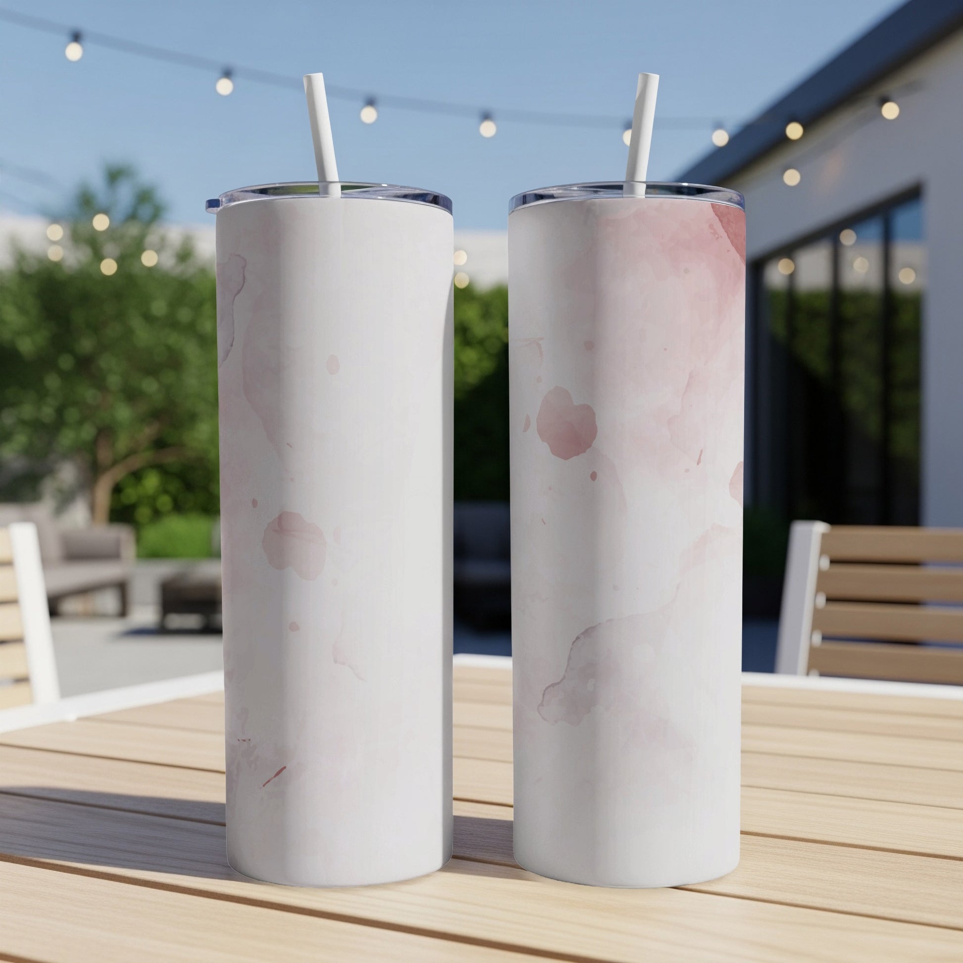 Two white tumblers with pink watercolor splotches, resting on a wooden table outdoors.