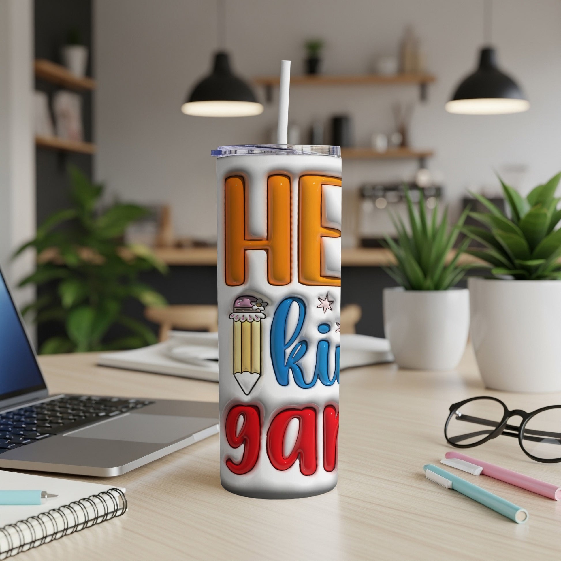 Tumbler with "HE kids gar" text and pencil graphic on a desk.