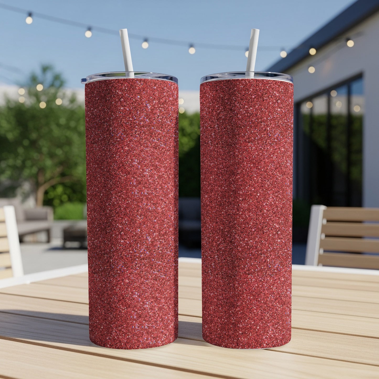 Two tall, skinny tumblers with red glitter finish and white straws sit on a wooden table.