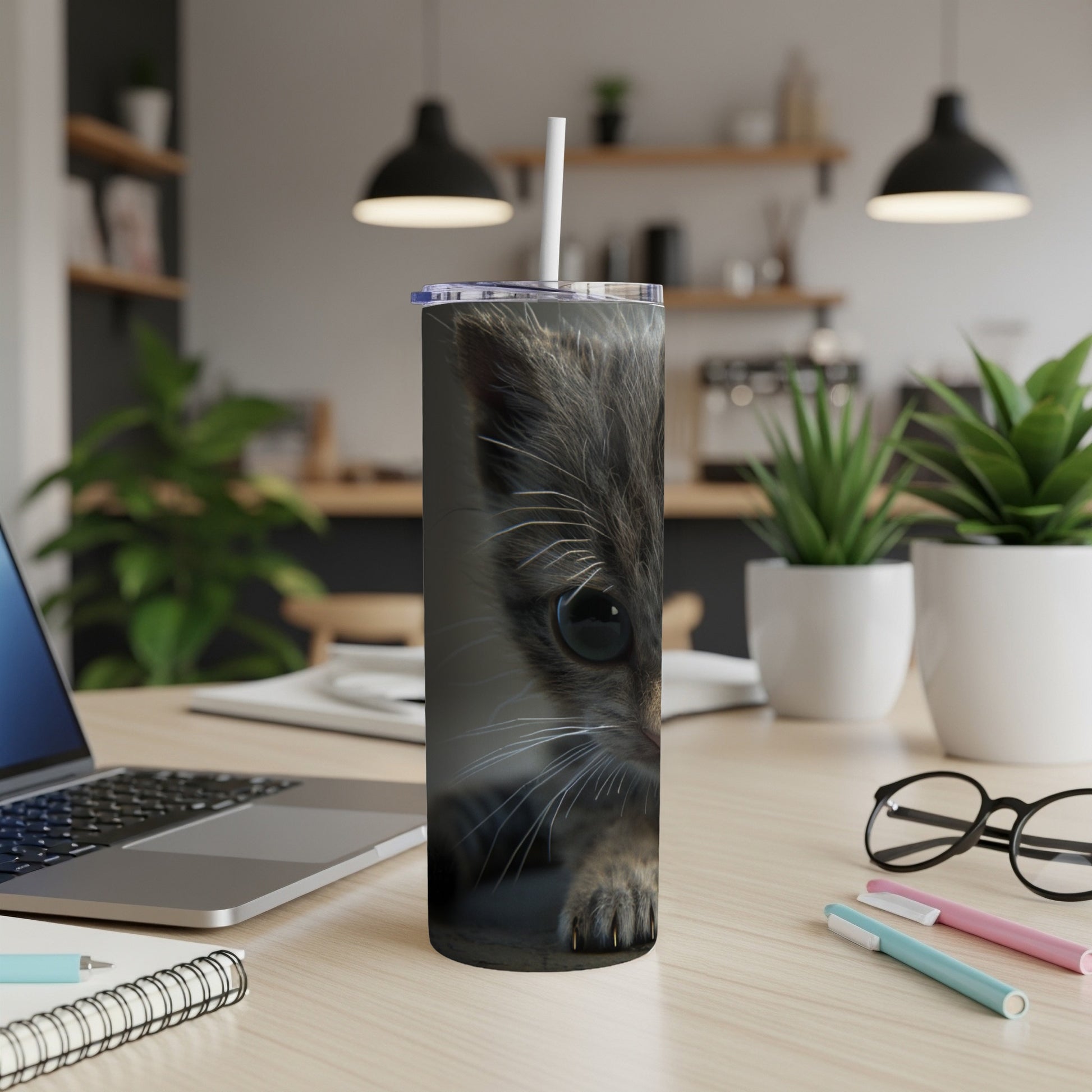 Close-up of a kitten's face on a tumbler, sitting on a desk.