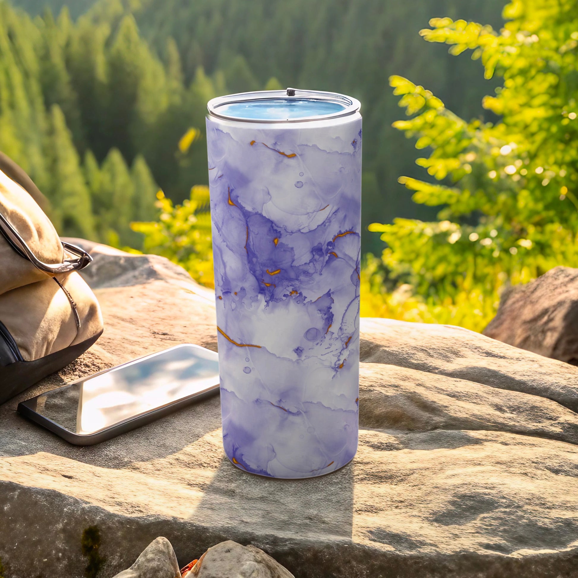 Purple and gold marble pattern tumbler with smartphone and backpack outdoors.