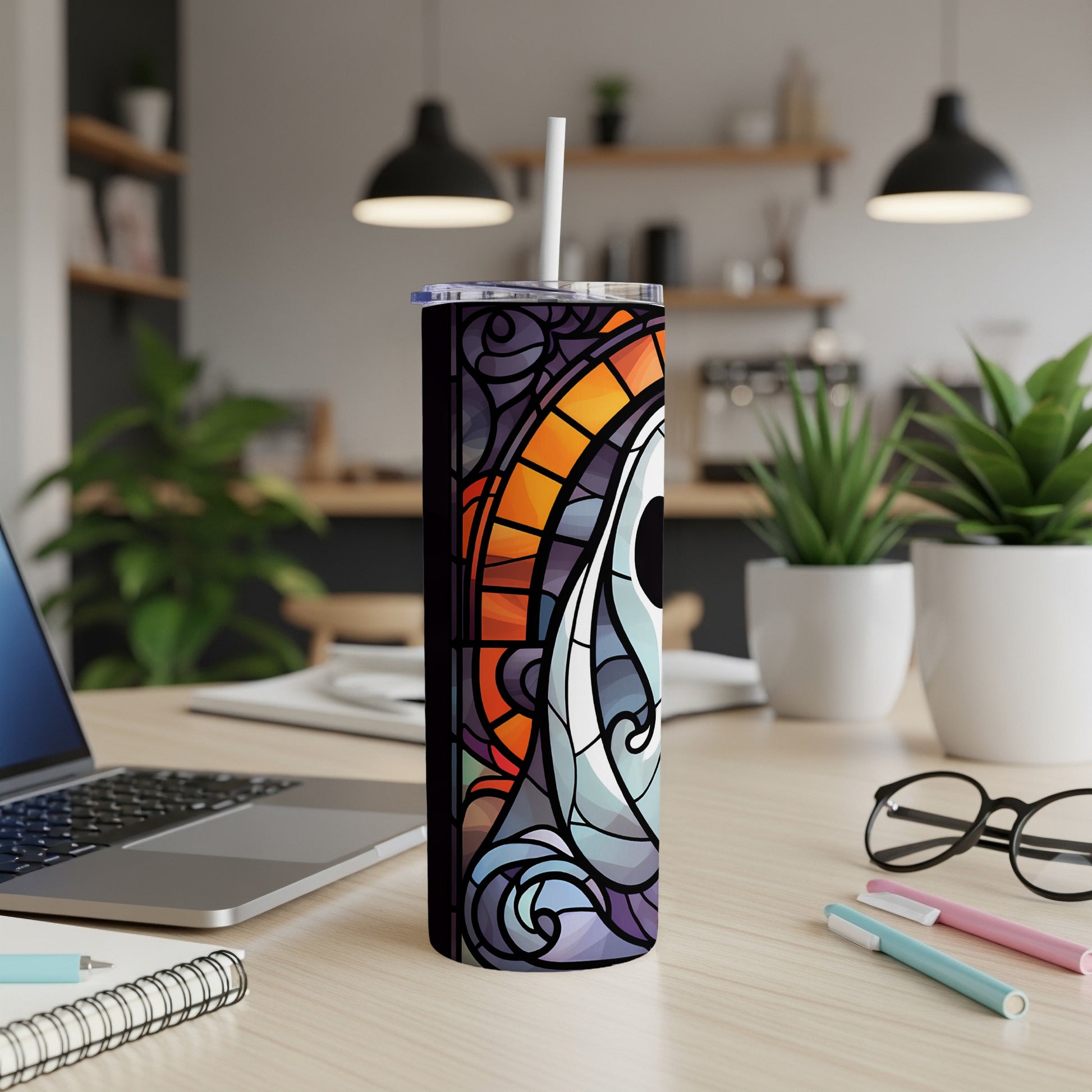 Stained glass tumbler with colorful eye design on desk with laptop and pens.