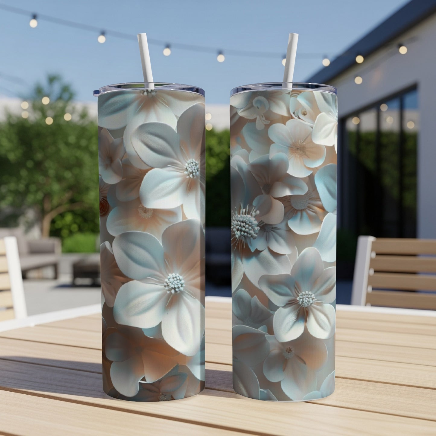 Two floral patterned tumblers with straws on a wooden table outdoors.