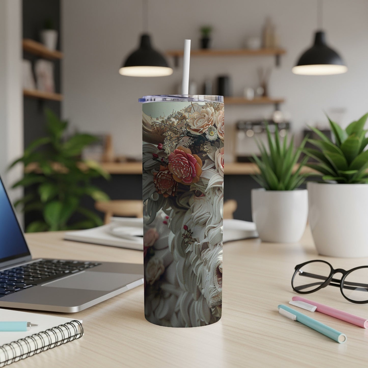 Floral-patterned tumbler with straw on a wooden desk with laptop.