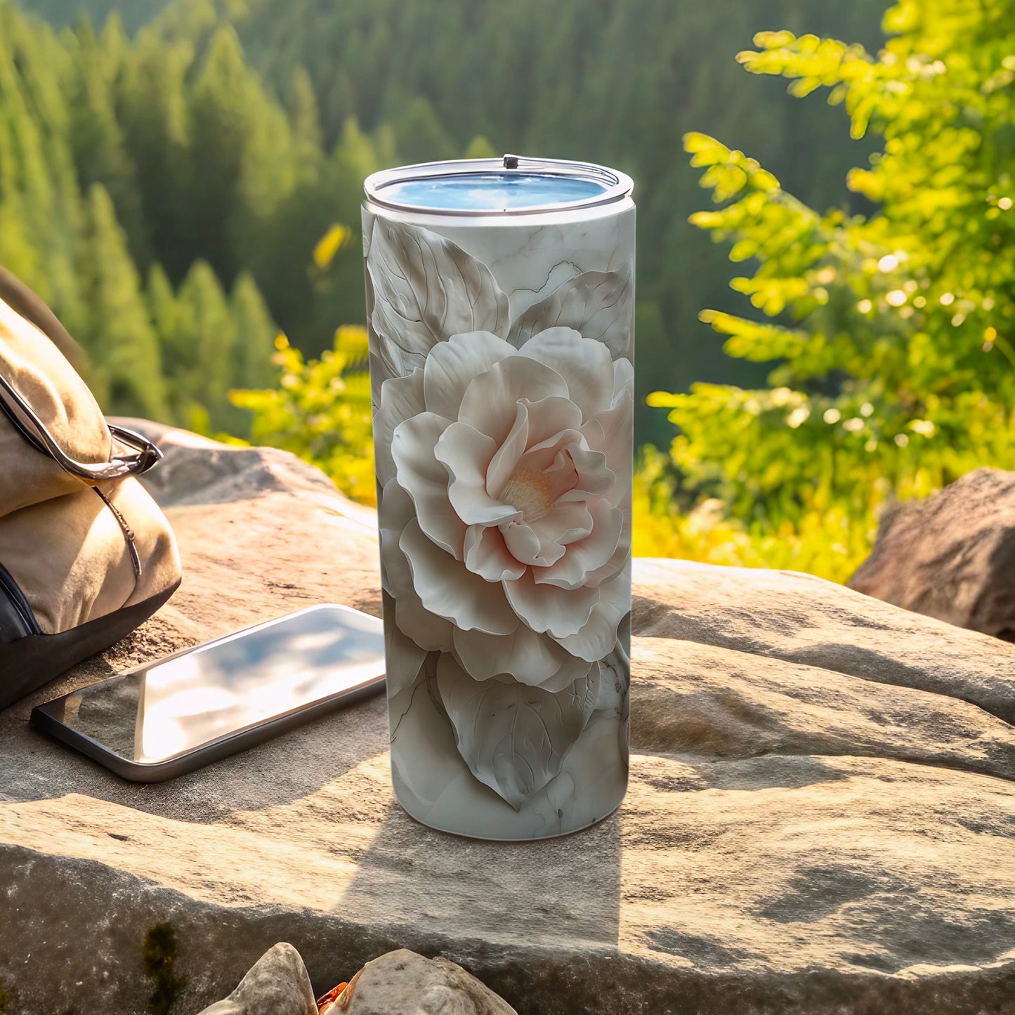 White floral design on a white tumbler, resting on rocks outdoors.