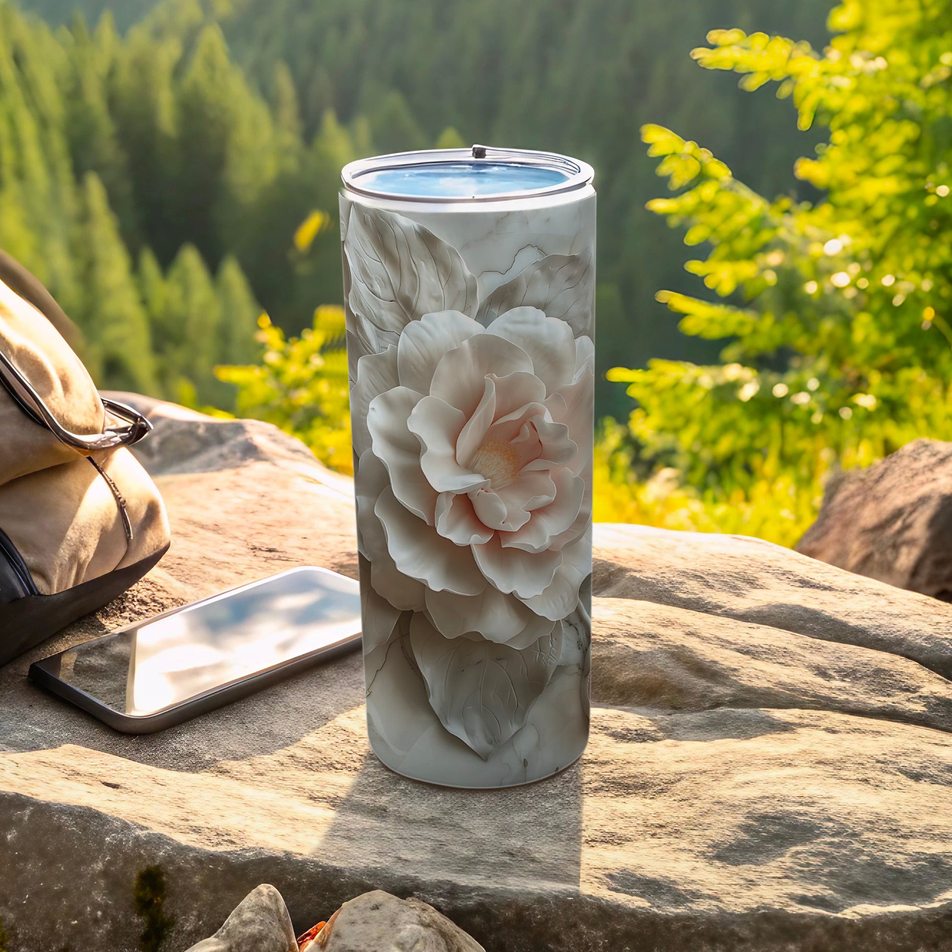 White floral design on a white tumbler, resting on rocks outdoors.