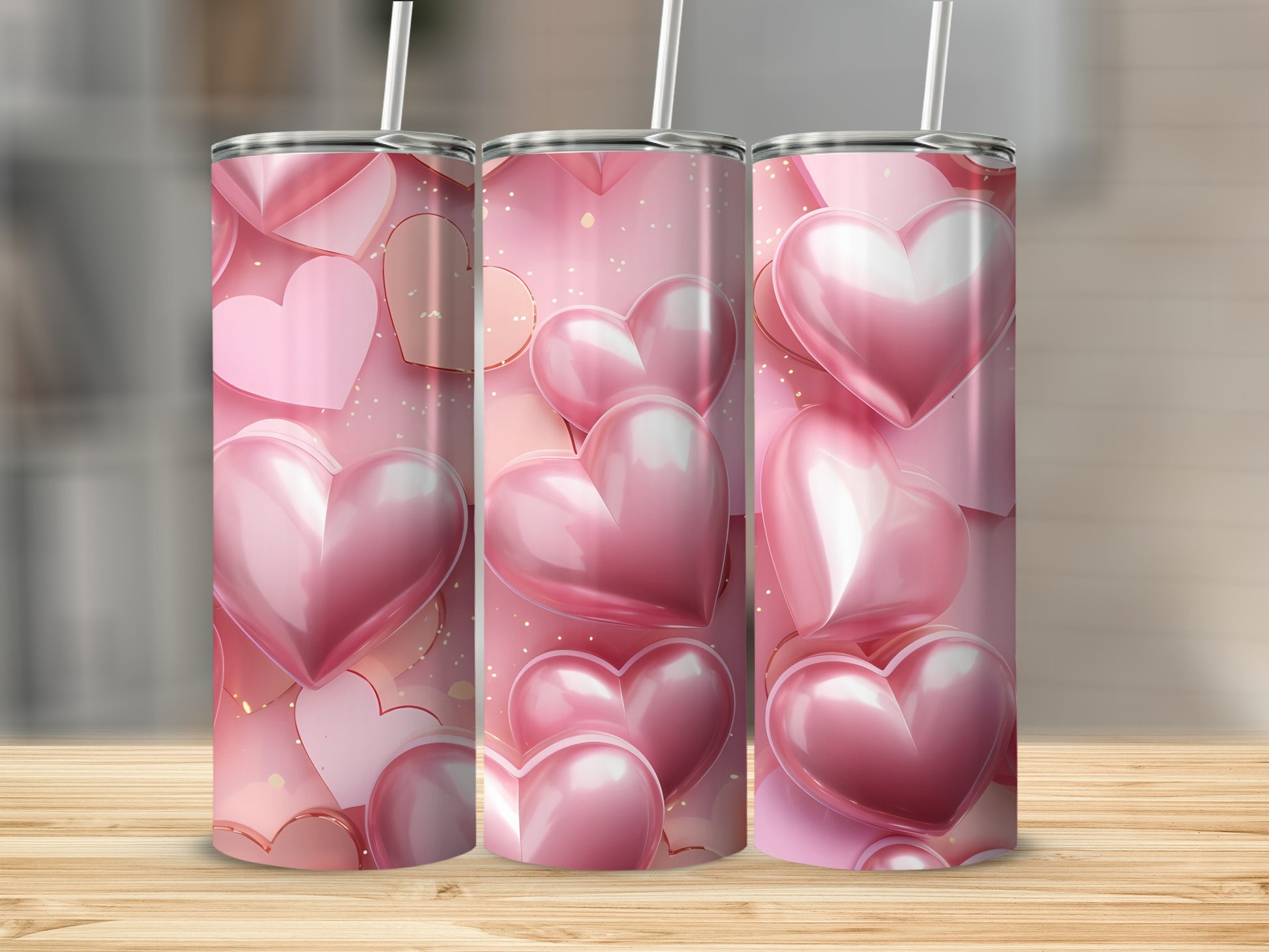 Three pink heart-covered tumblers with straws on a wooden surface.
