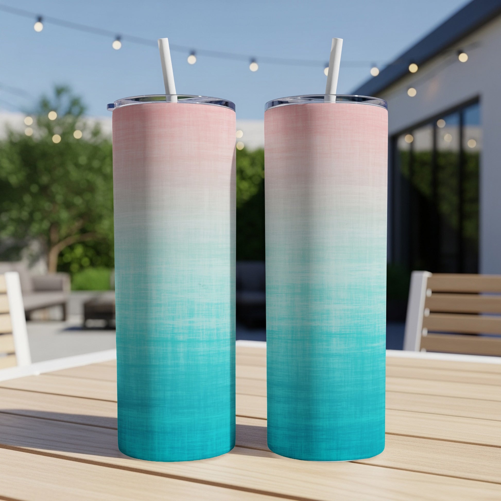 Two tall tumblers with pink and teal ombre design and straws on a table.