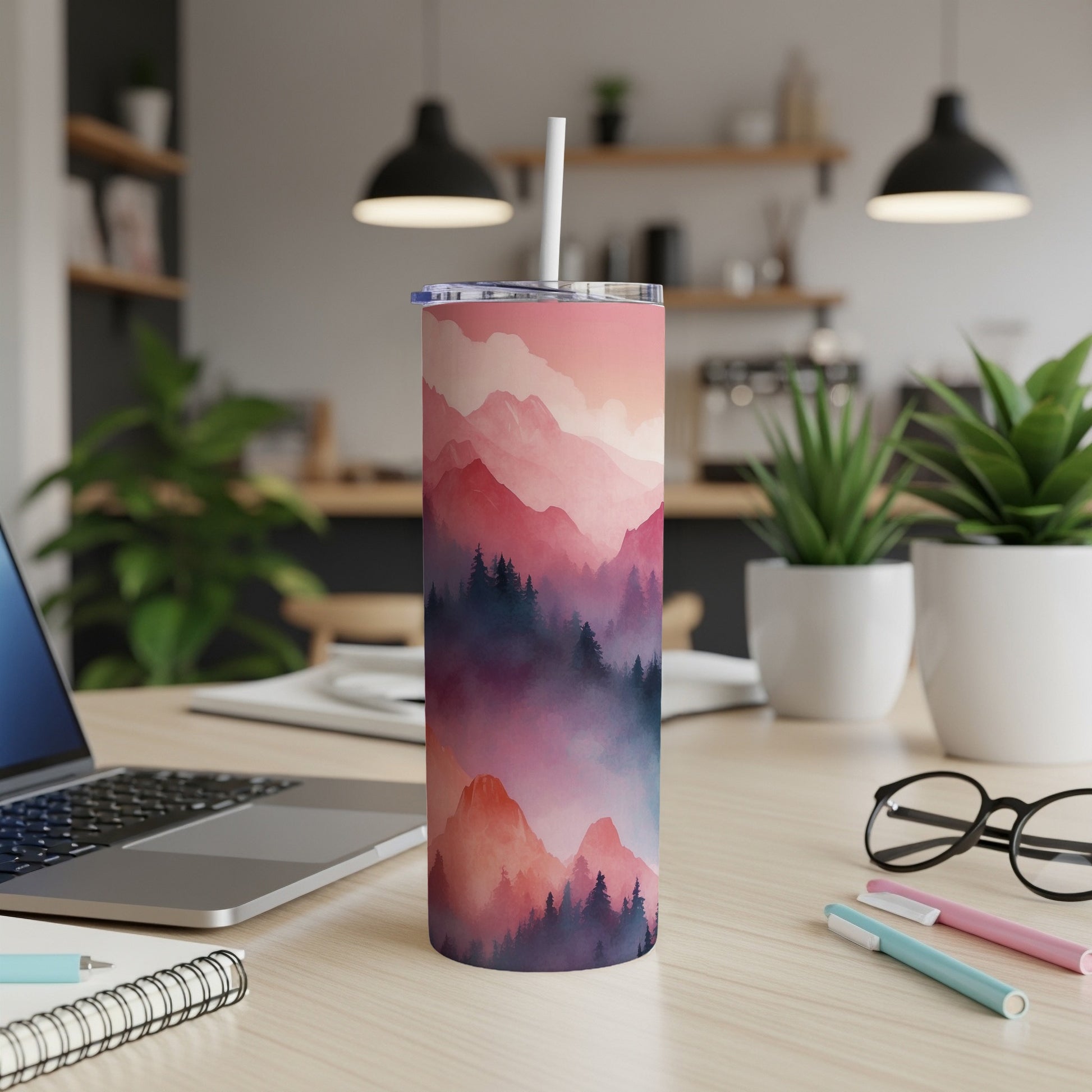 Pink and purple mountain landscape tumbler with straw on a desk.