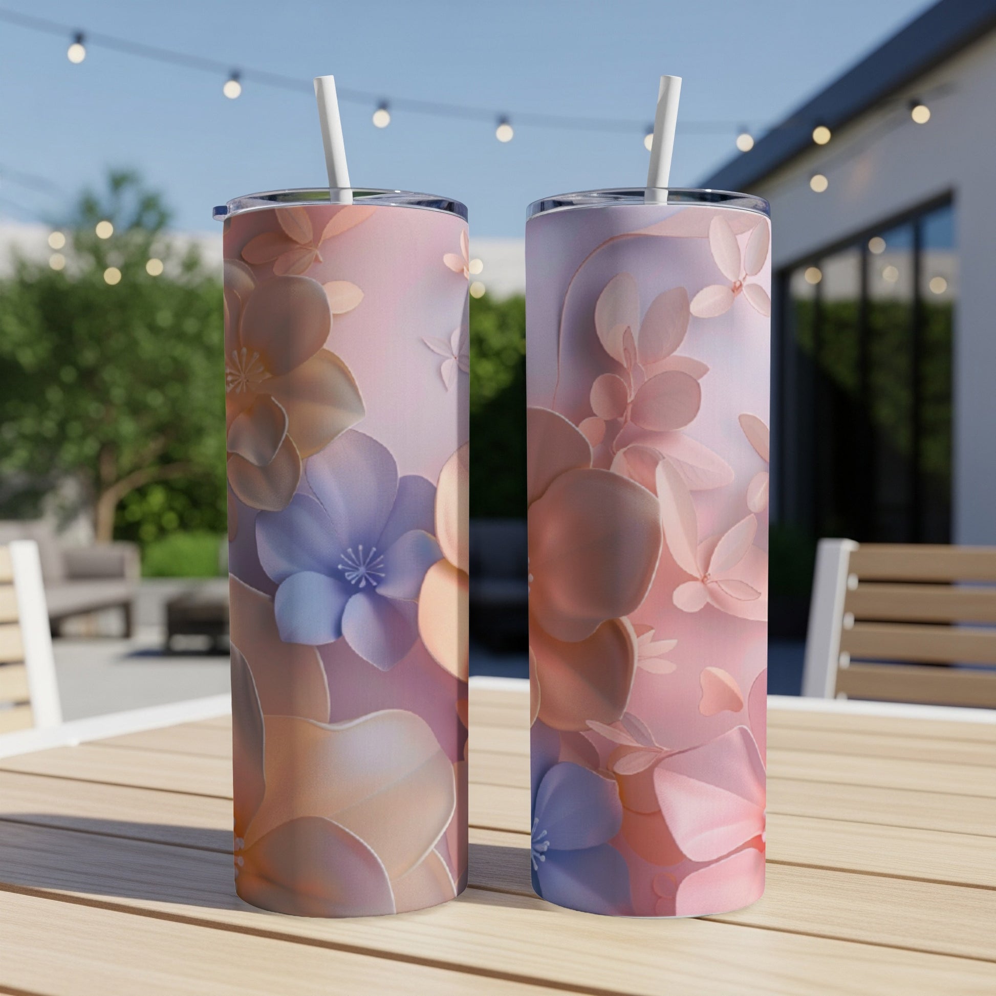 Two tall tumblers with a floral and leaf pattern on an outdoor table.