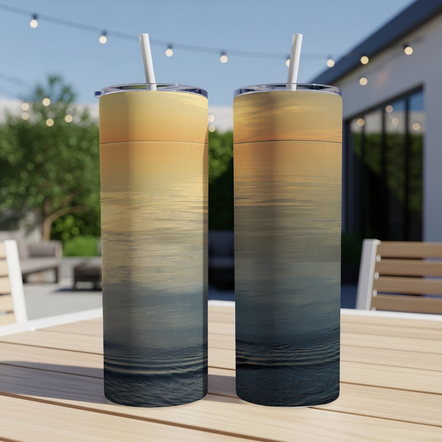 Two tumblers with a sunset over water scene on an outdoor table.