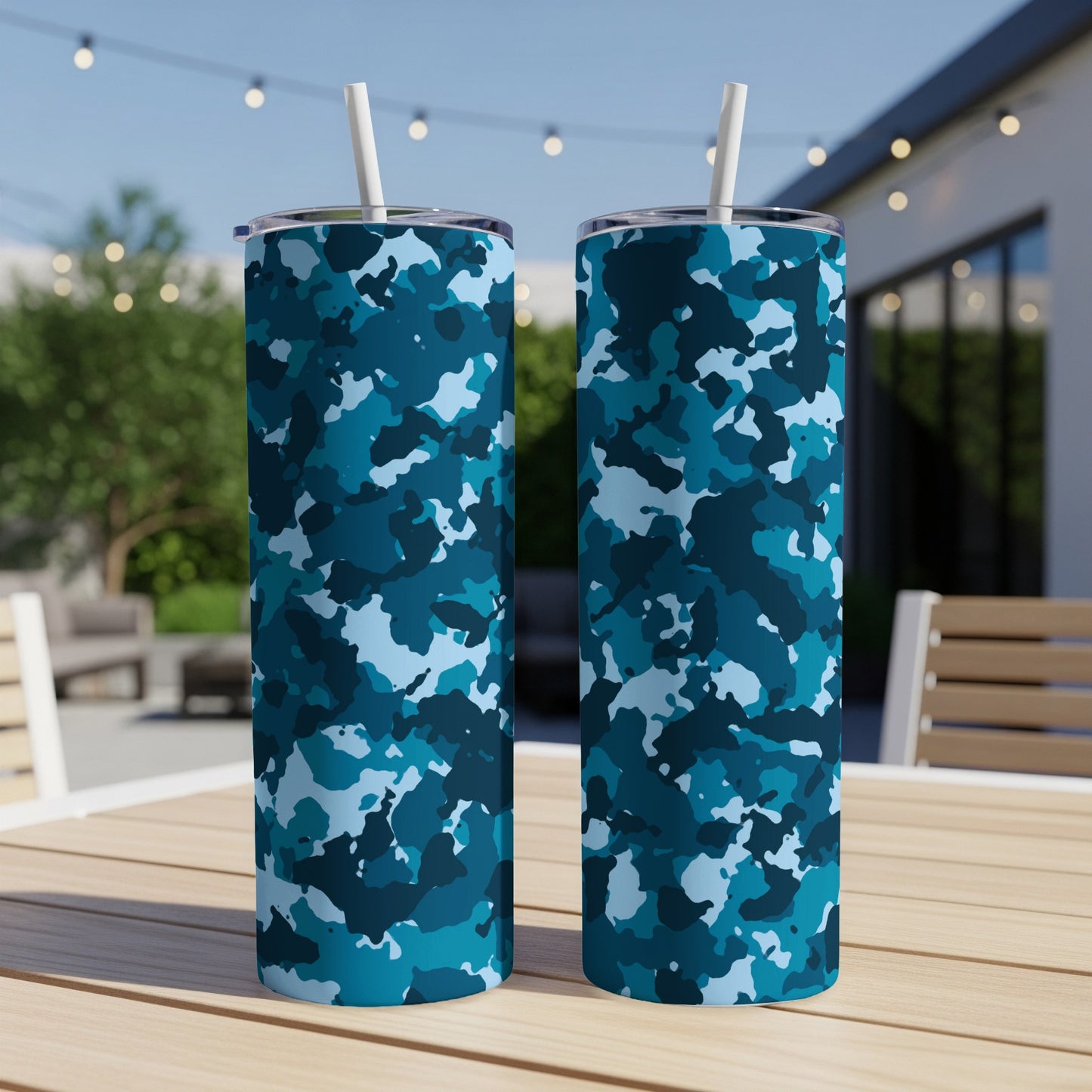 Two blue camouflage tumblers with straws on a wooden table outdoors.