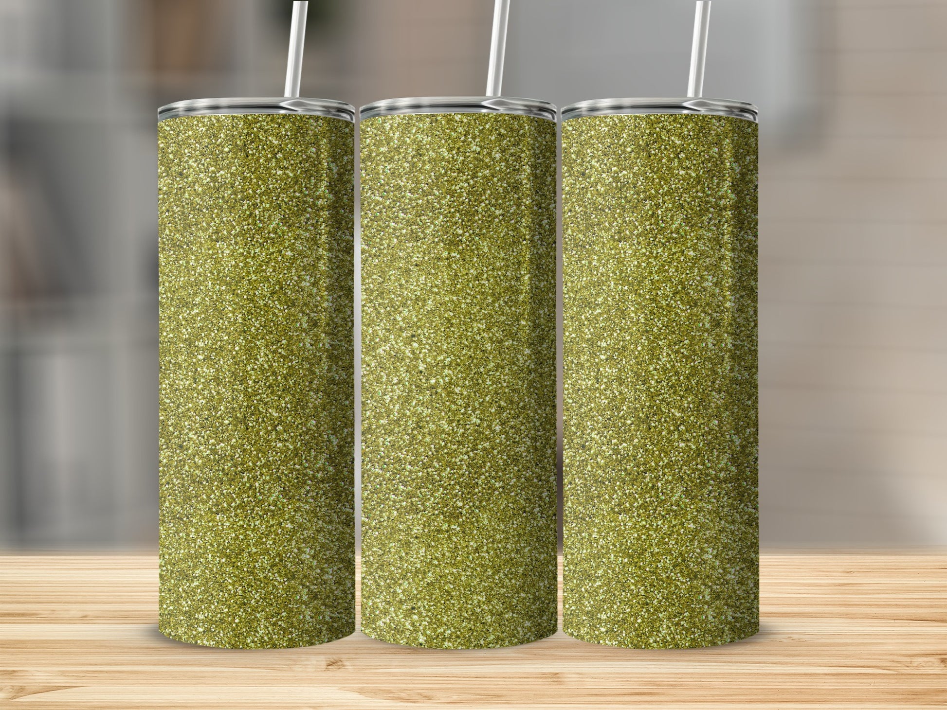 Three tall, glittery, gold tumblers with straws on a wooden surface.