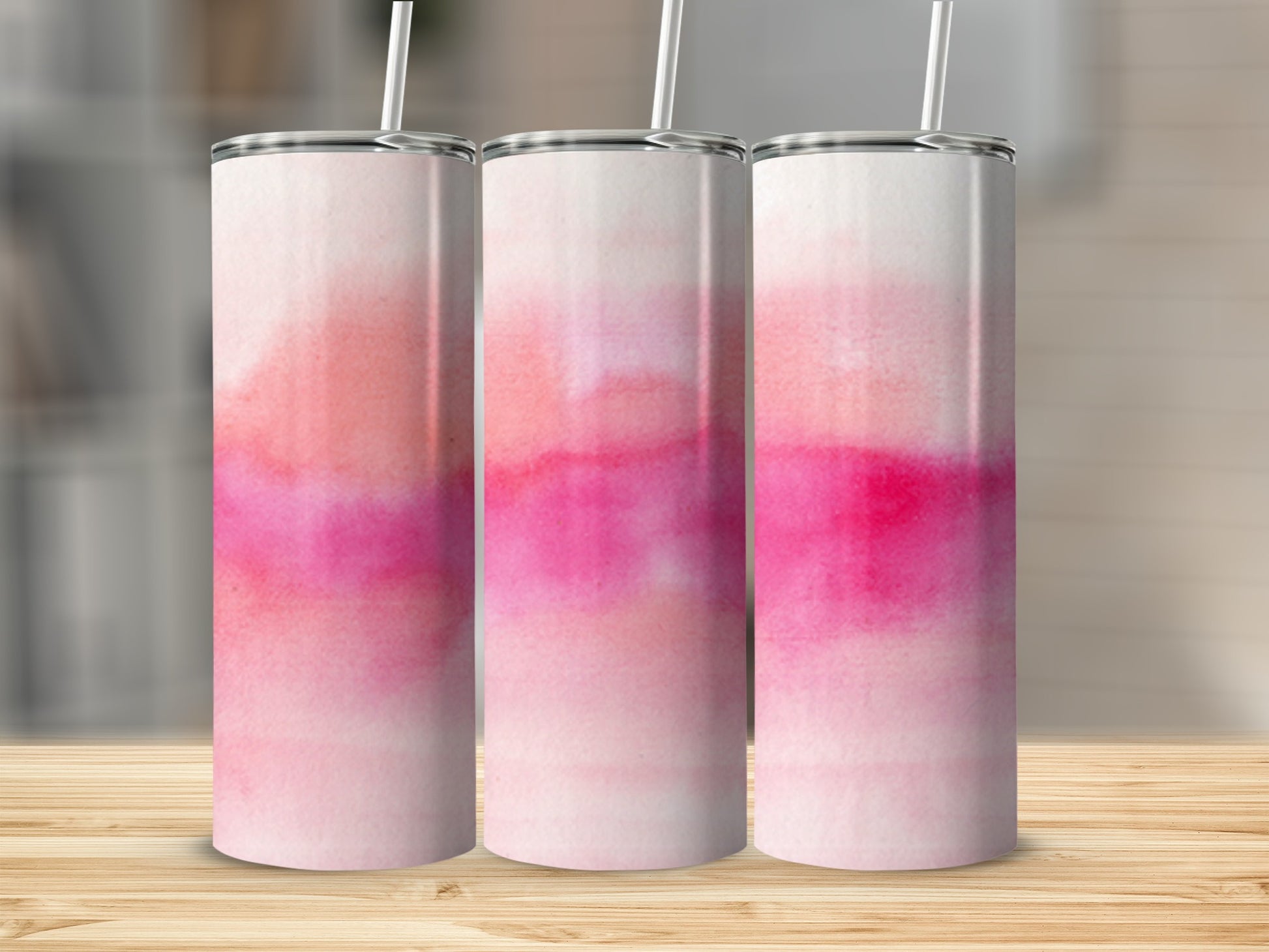 Three pink and white watercolor tumblers with straws on a wooden surface.