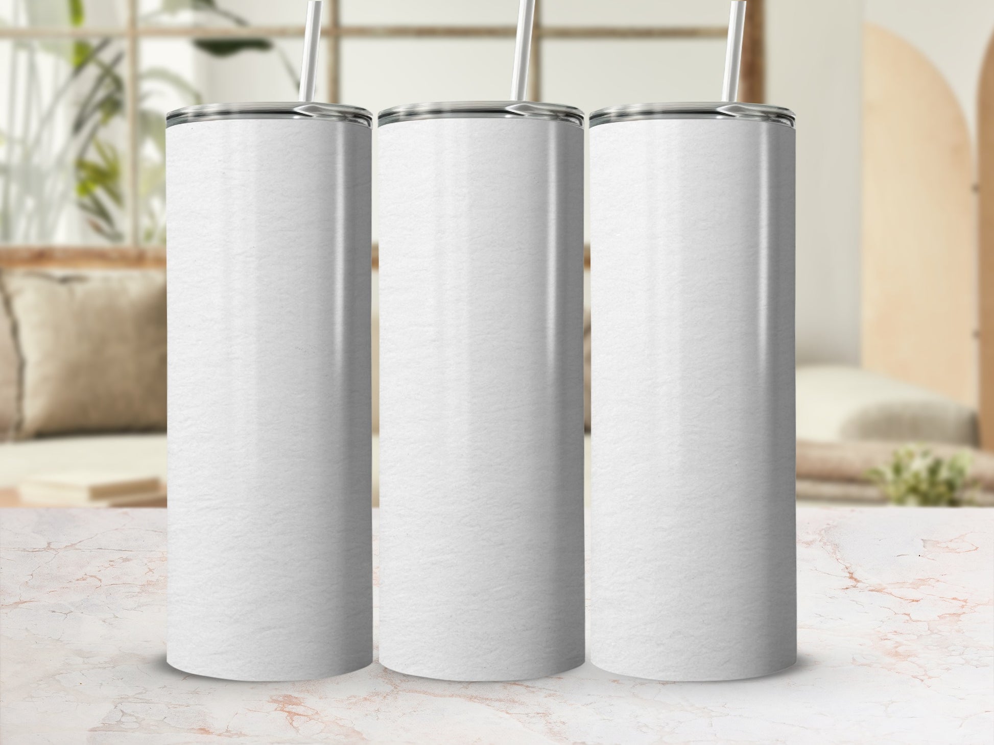 Three blank white tumblers with straws on a marble countertop.
