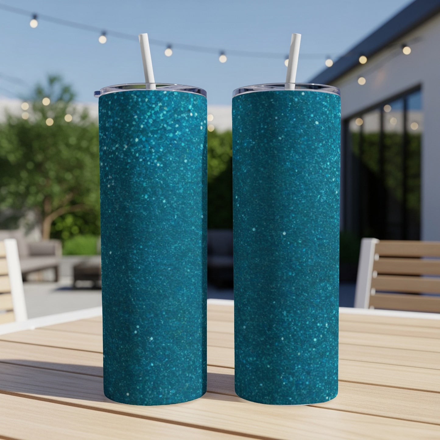 Two teal glitter tumblers with straws sit on a wooden table outdoors.
