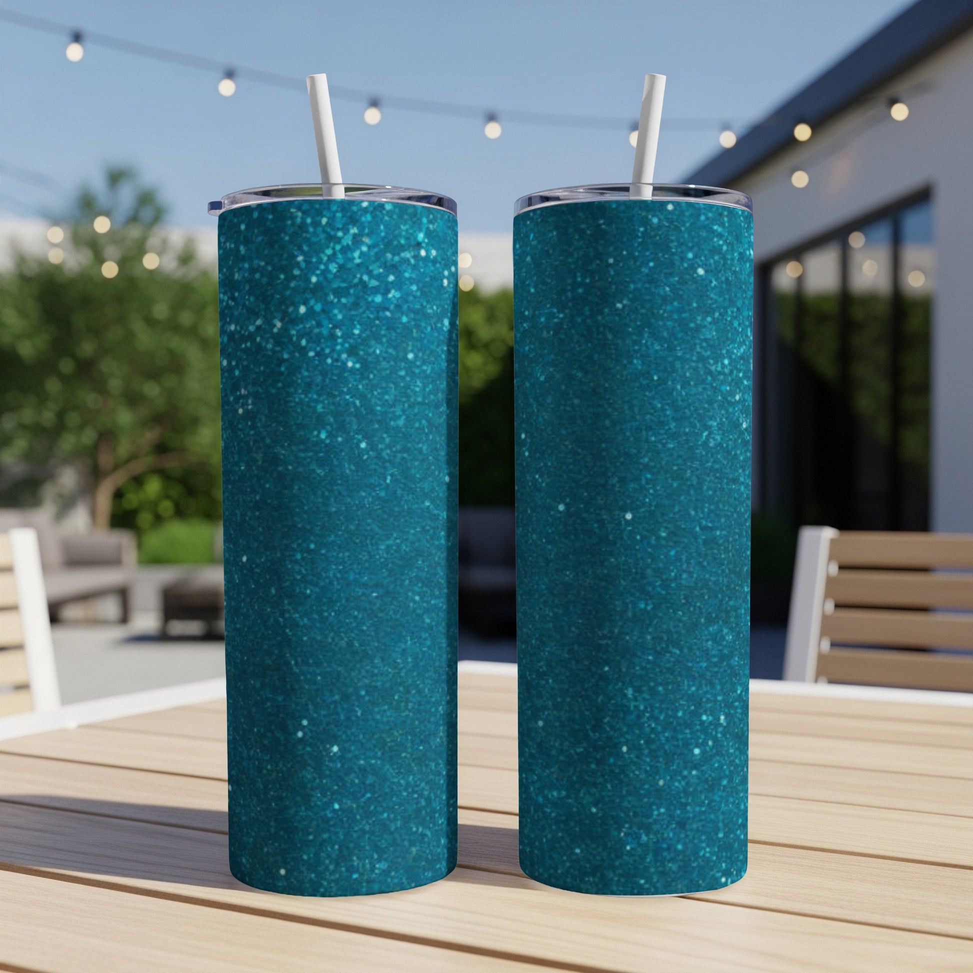 Two teal glitter tumblers with straws sit on a wooden table outdoors.