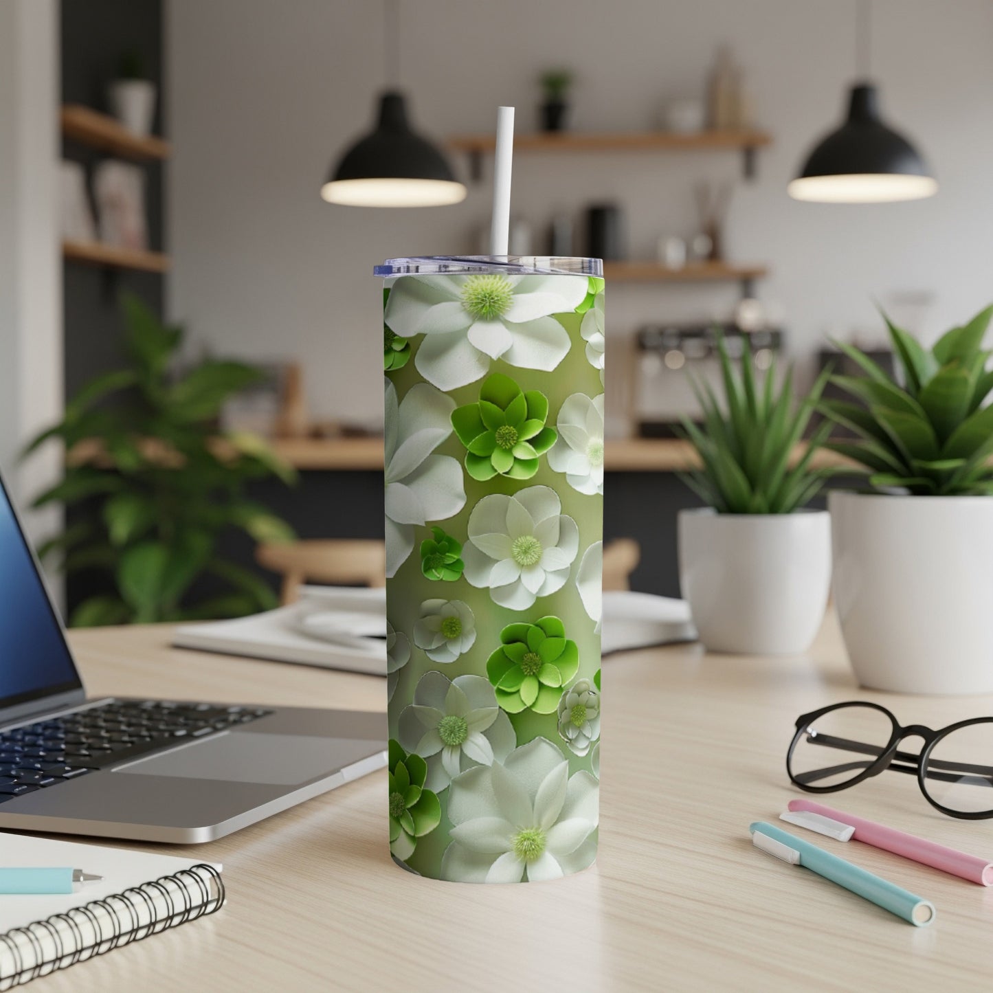 Green tumbler with white and green floral pattern on desk.