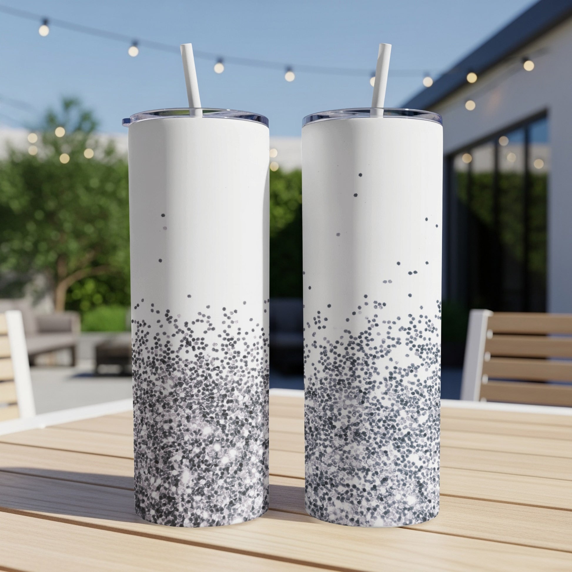 Two tall, white tumblers with silver glitter ombre design, outdoor setting.
