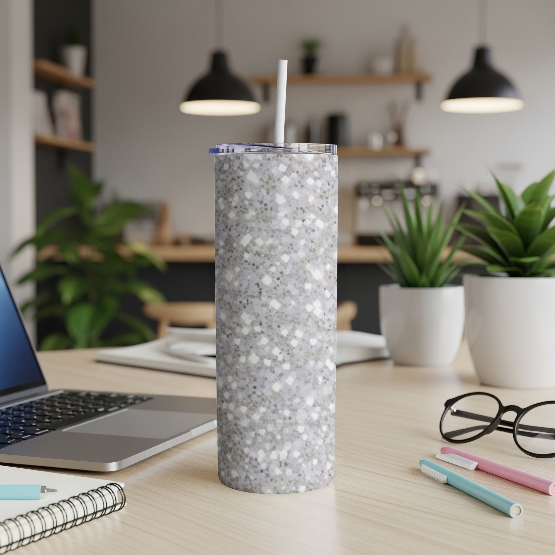 Glittery grey tumbler with a white straw on a wooden desk.