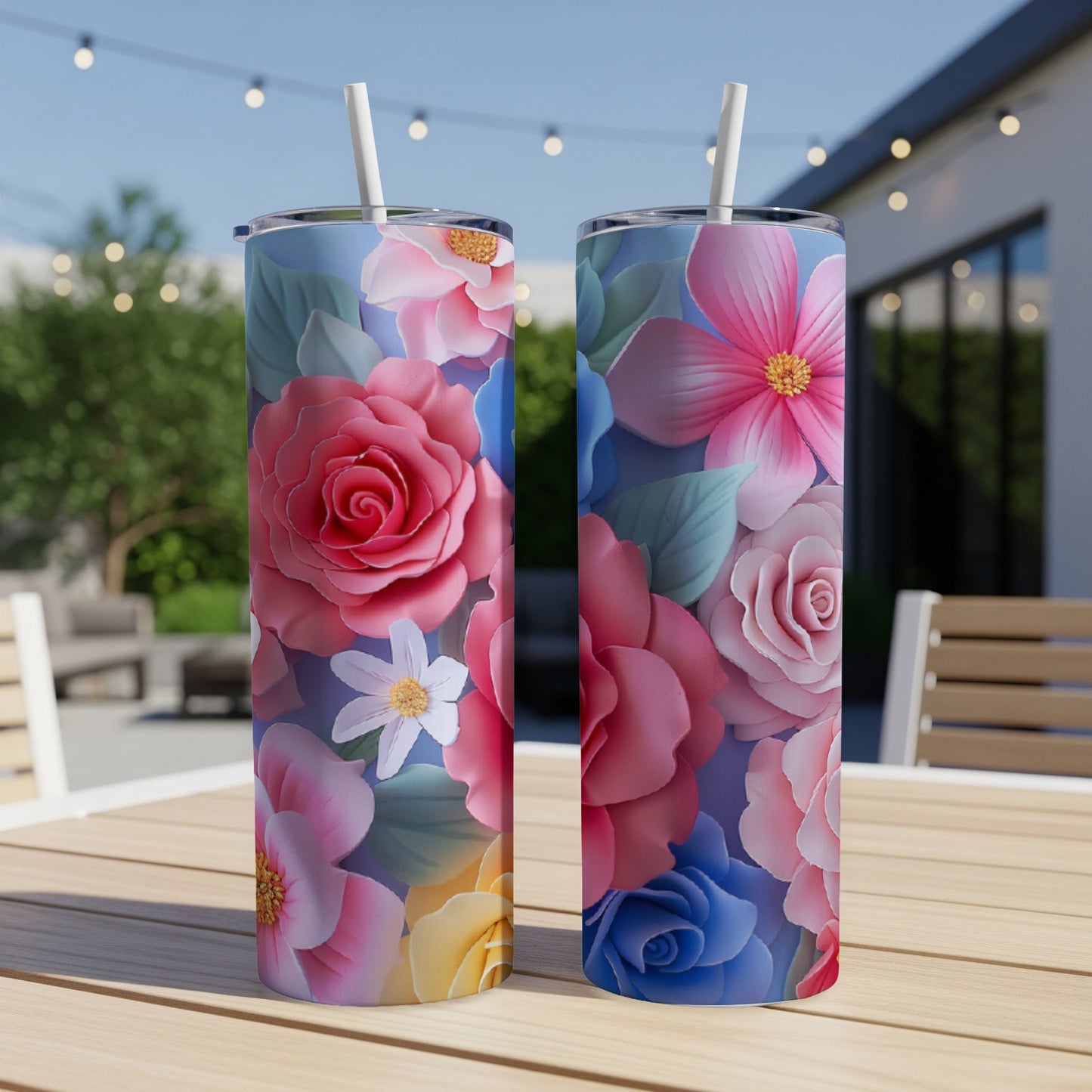 Two tall, floral-patterned tumblers with straws on a wooden table outdoors.