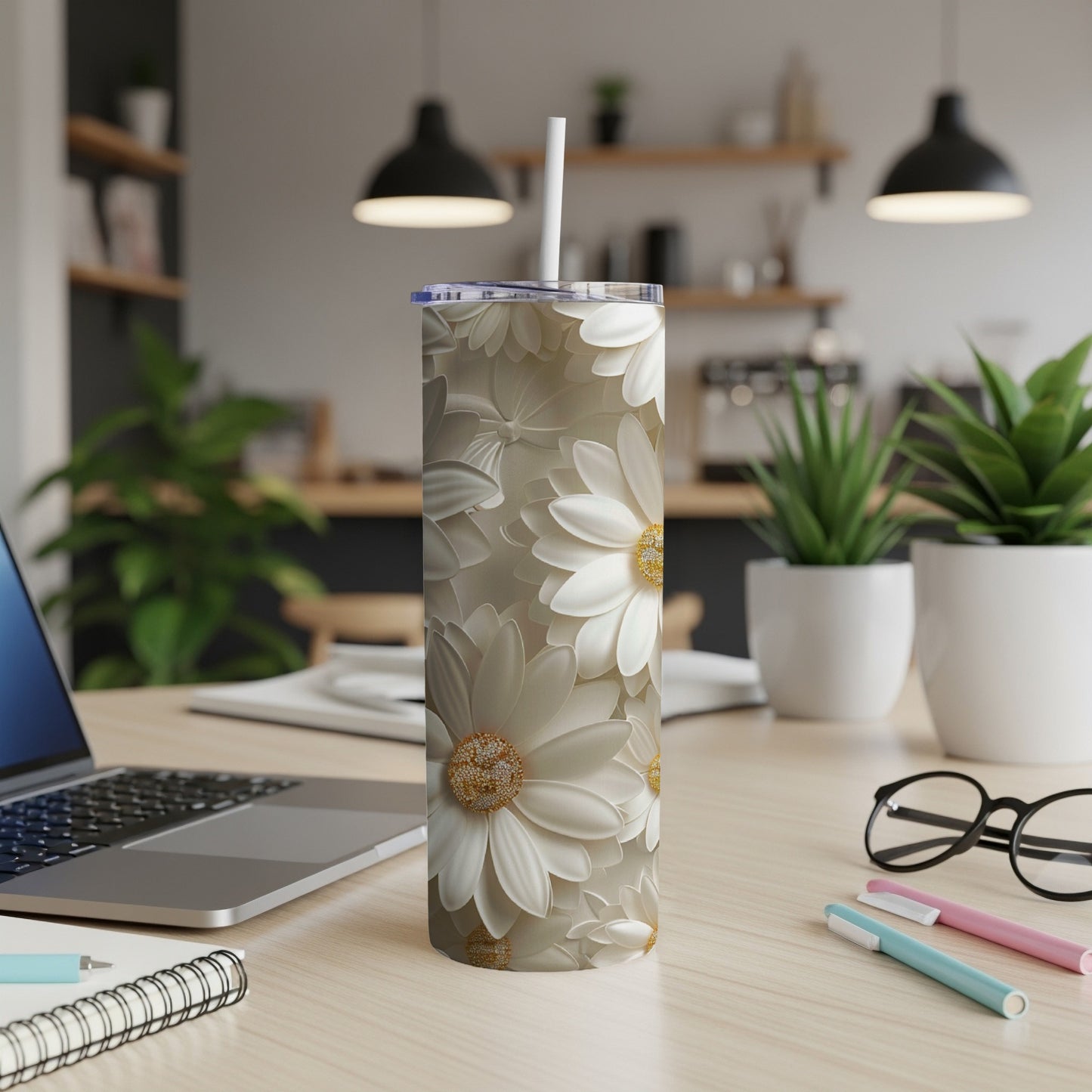 White daisy pattern on a slim, white tumbler with a straw, on a desk.