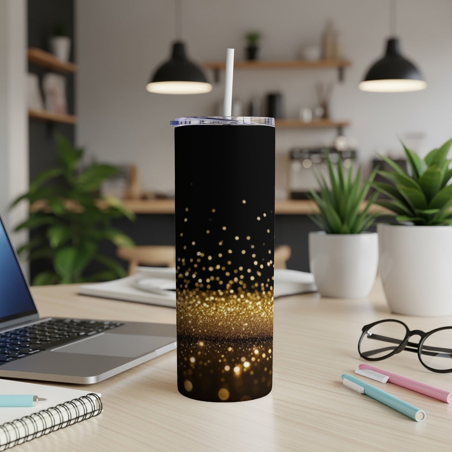 Black tumbler with gold glitter design and white straw on a desk.