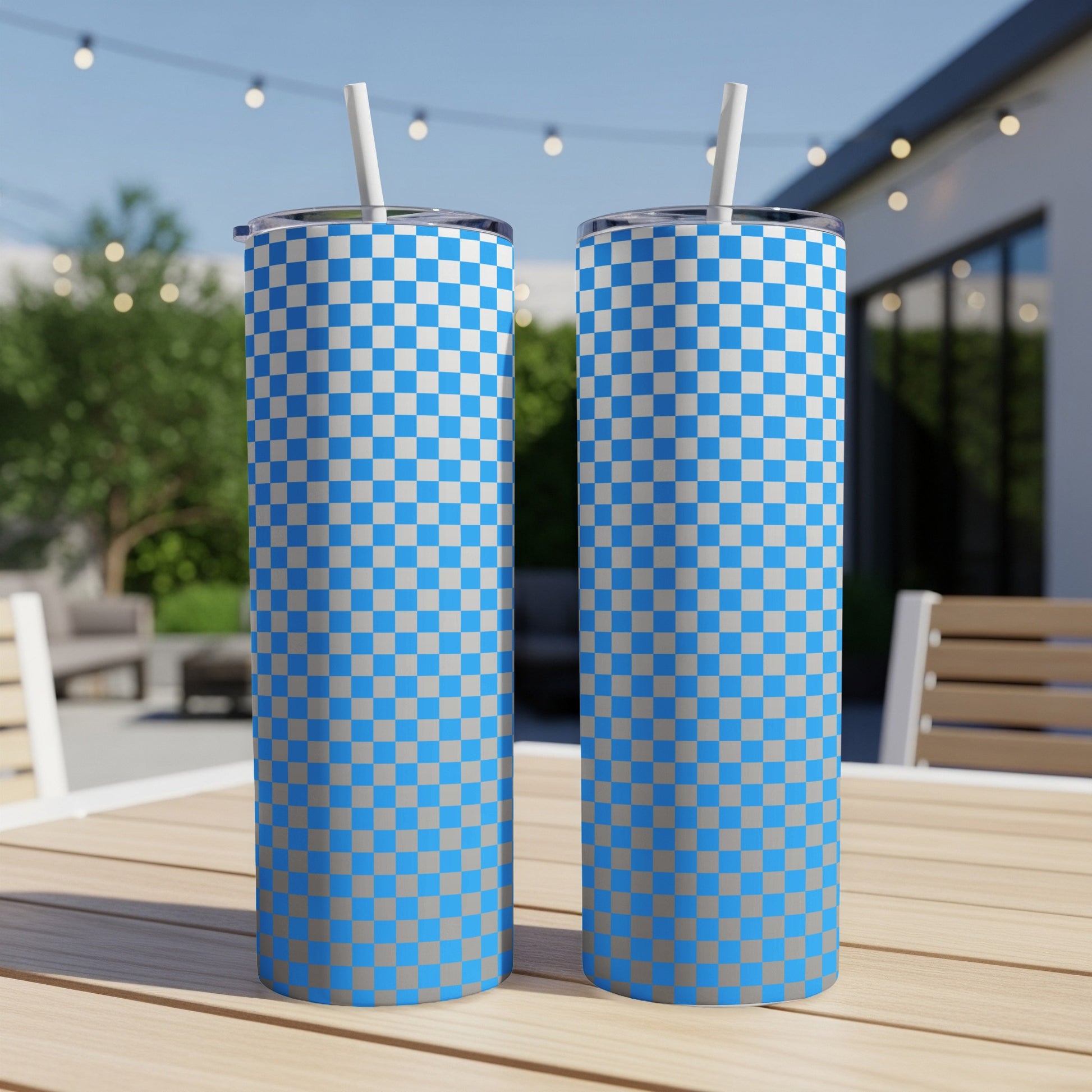 Two blue and gray checkered tumblers with straws on a wooden table outdoors.