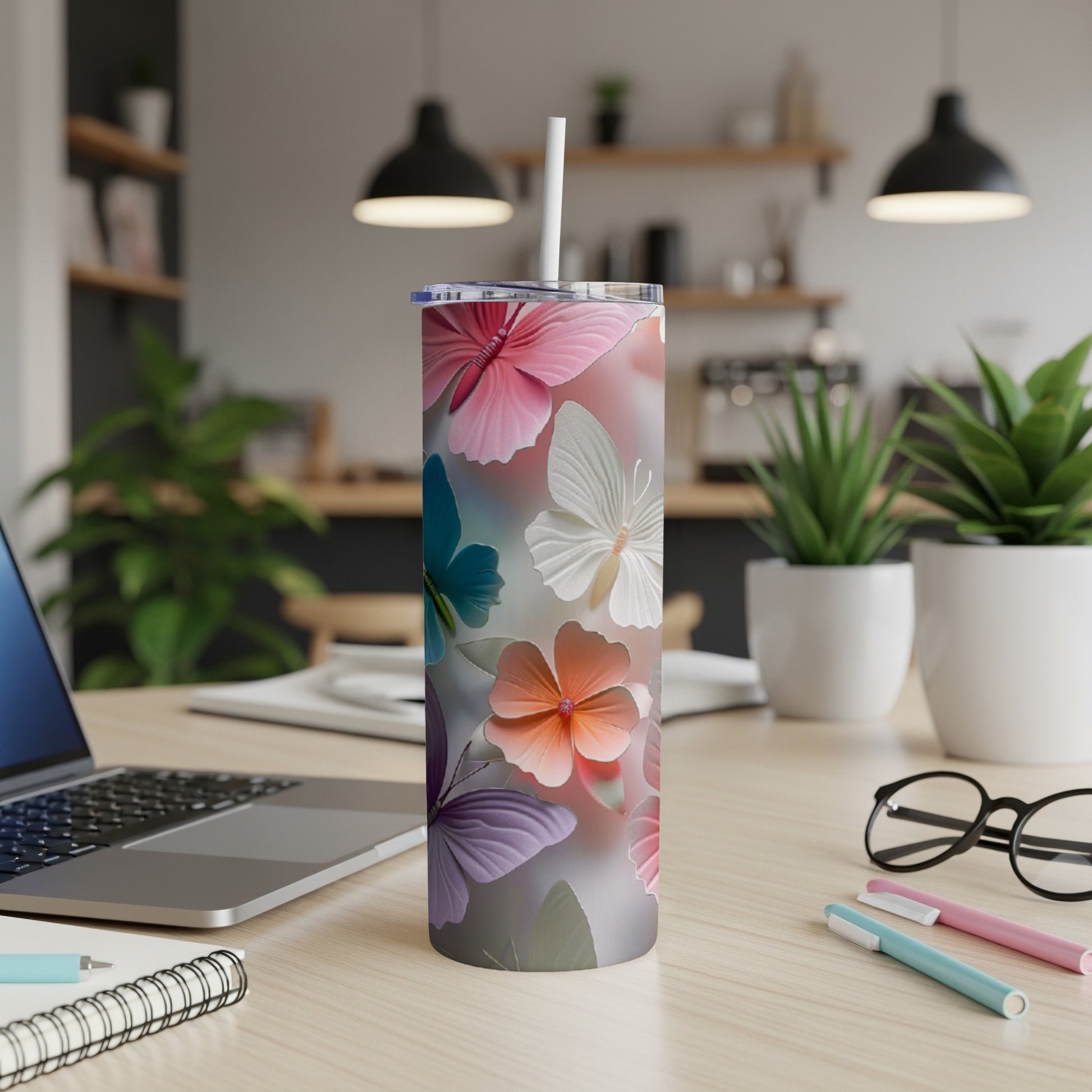 Tumbler with colorful butterfly pattern on a desk next to a laptop.