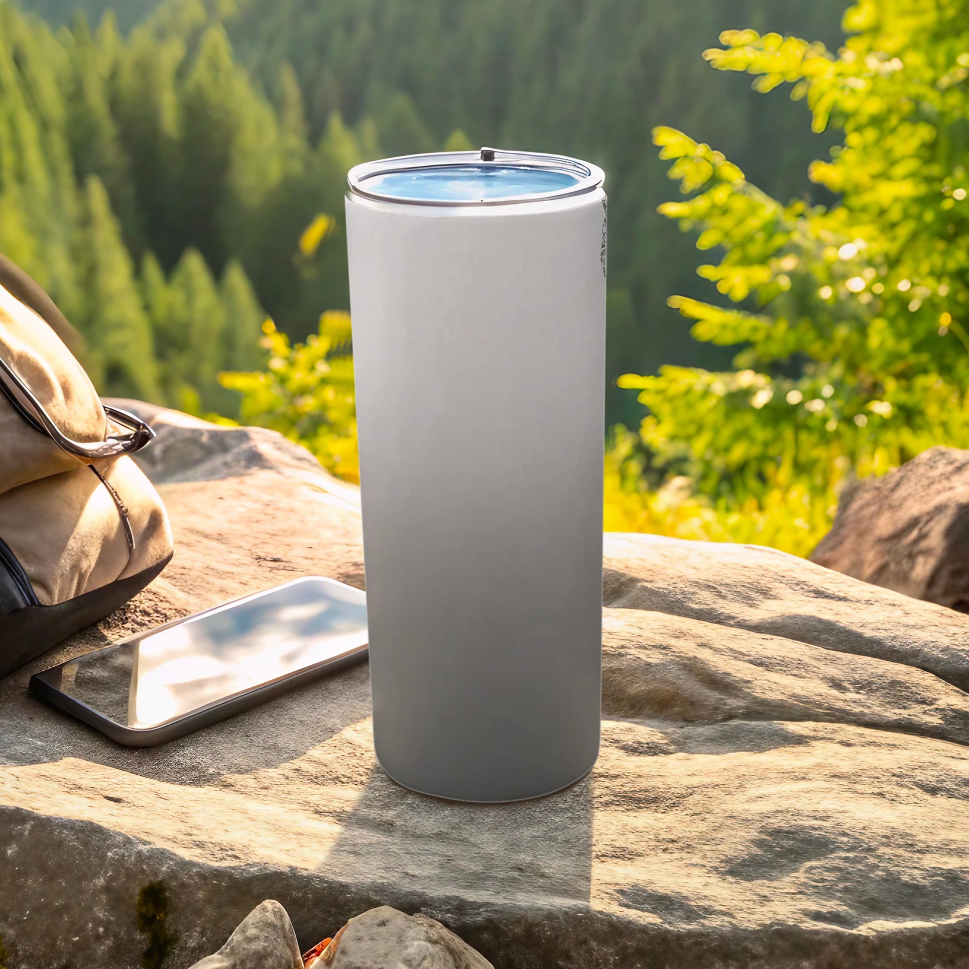 White and gray gradient tumbler on rock with phone and backpack.