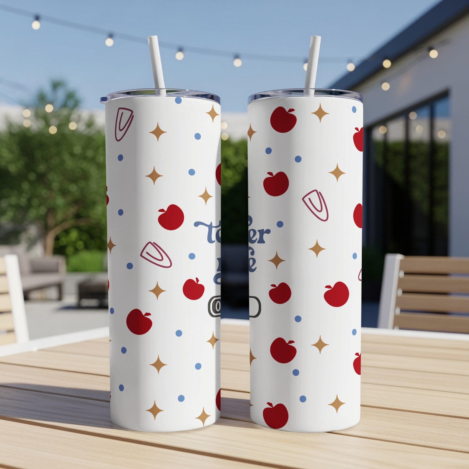 Two patterned tumblers with apples and stars on an outdoor table.