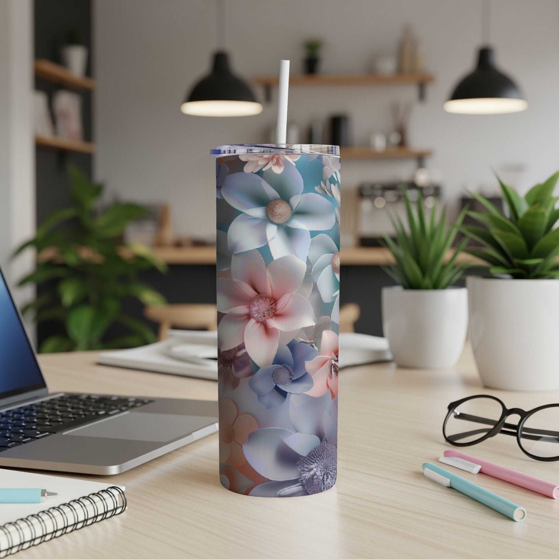 Floral tumbler with straw on a desk with a laptop and pens.
