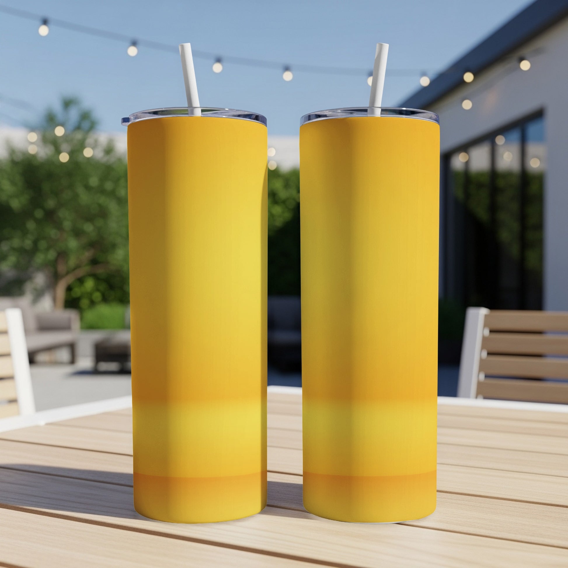 Two yellow gradient tumblers with straws on a wooden table outdoors.